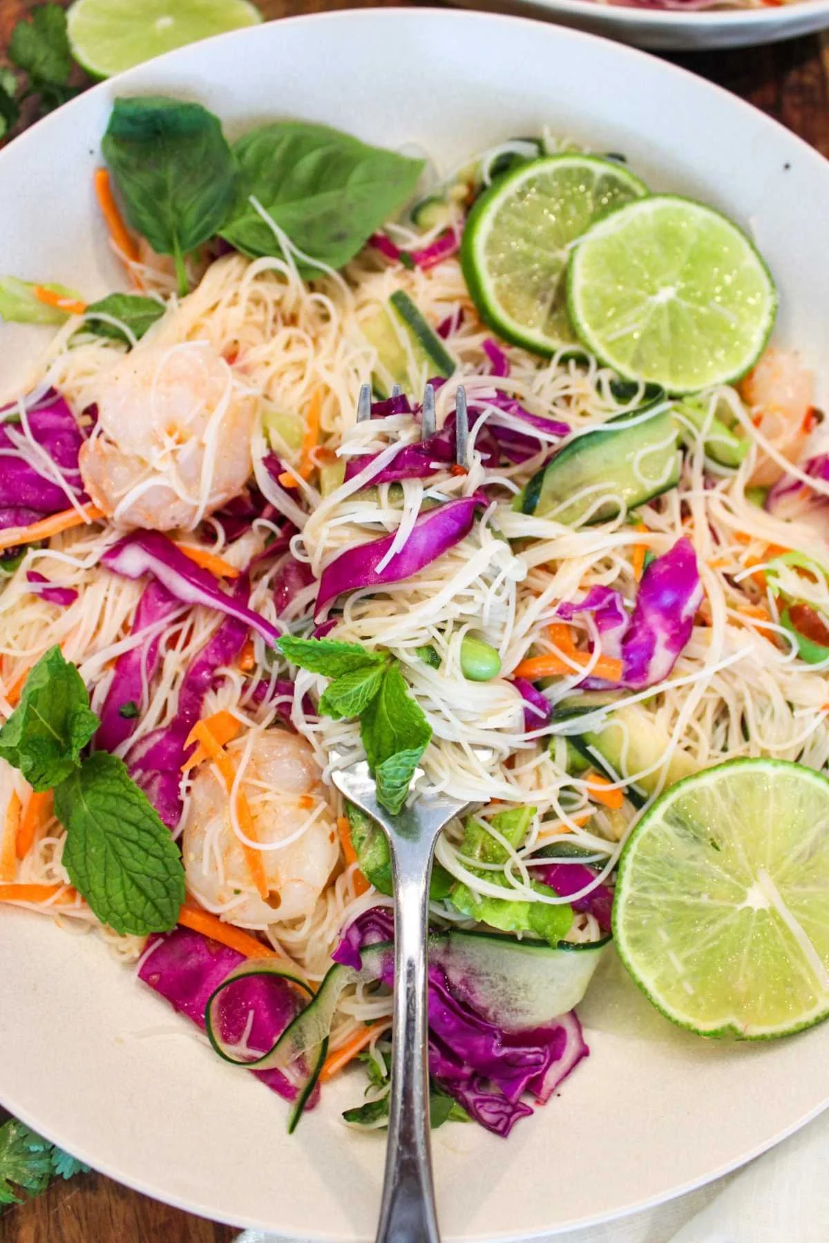 forkful of twisted spring roll in a bowl bite that features colorful ingredients like fresh limes, purple cabbage, shredded carrots, and cucumber ribbons for a refreshing bite.