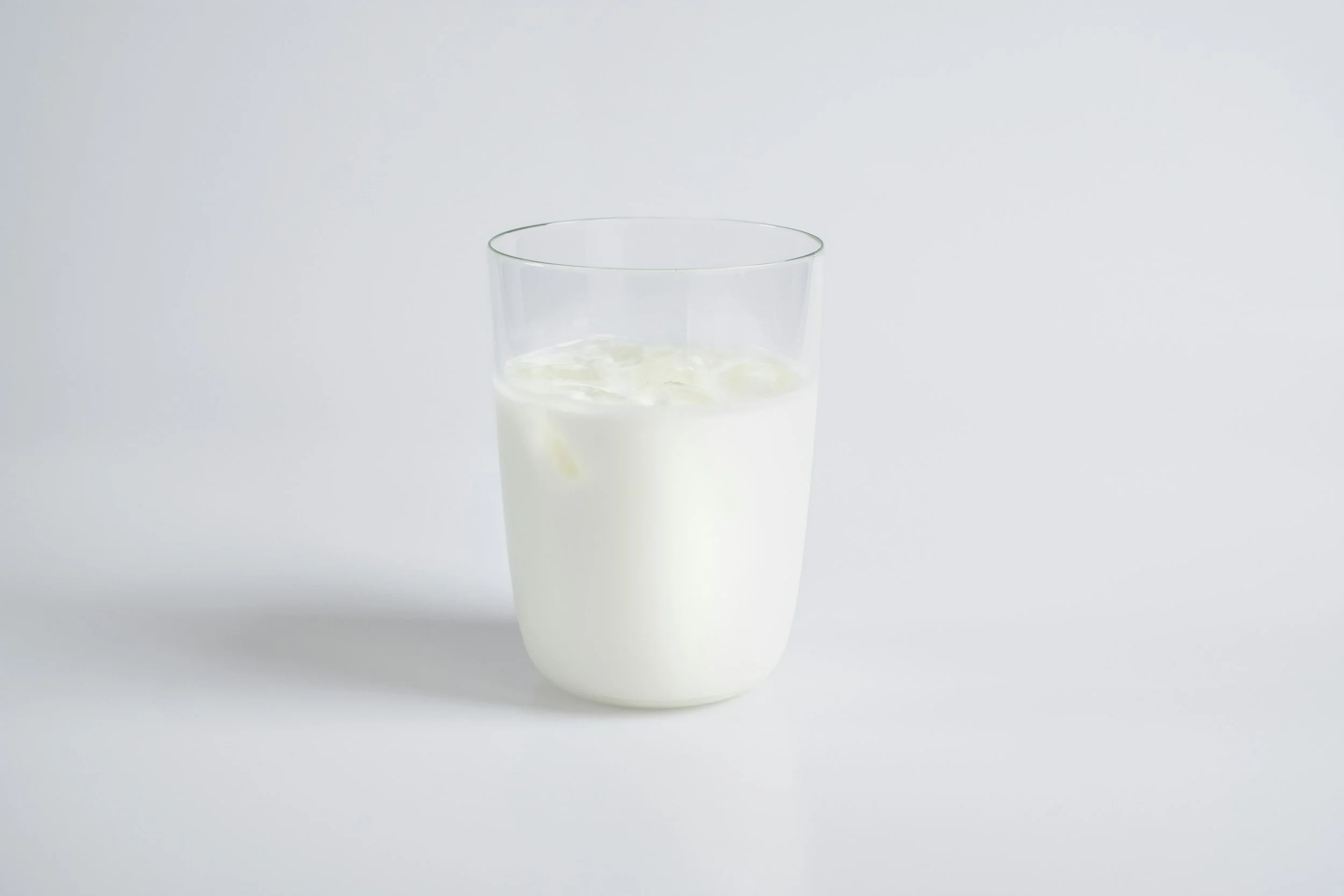 glass of milk with ice in it on a white table depicting a clean and clear image of milk.