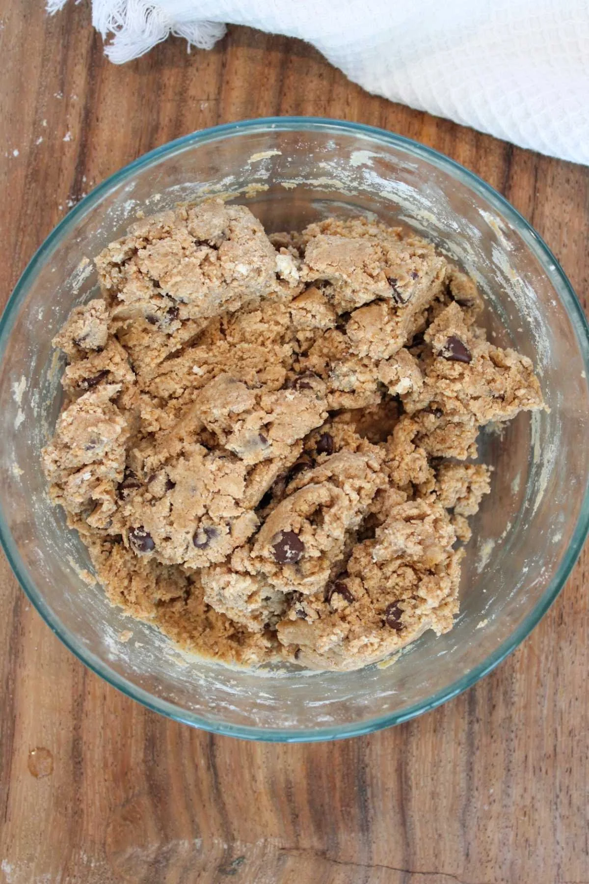 Bowl of protein cookie dough with chocolate chips, resting on a wooden surface. The texture looks chunky and ready for baking, creating a cozy, homemade vibe.