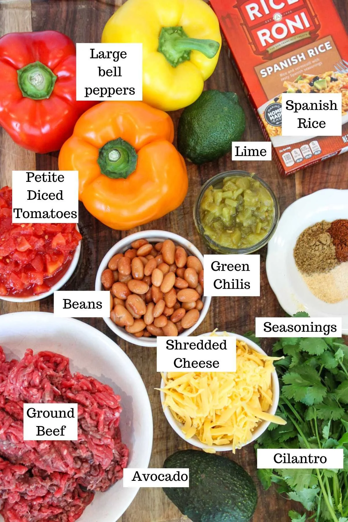 A variety of ingredients for a Mexican-inspired dish include bell peppers, diced tomatoes, beans, ground beef, cheese, avocado, lime, rice, and spices.