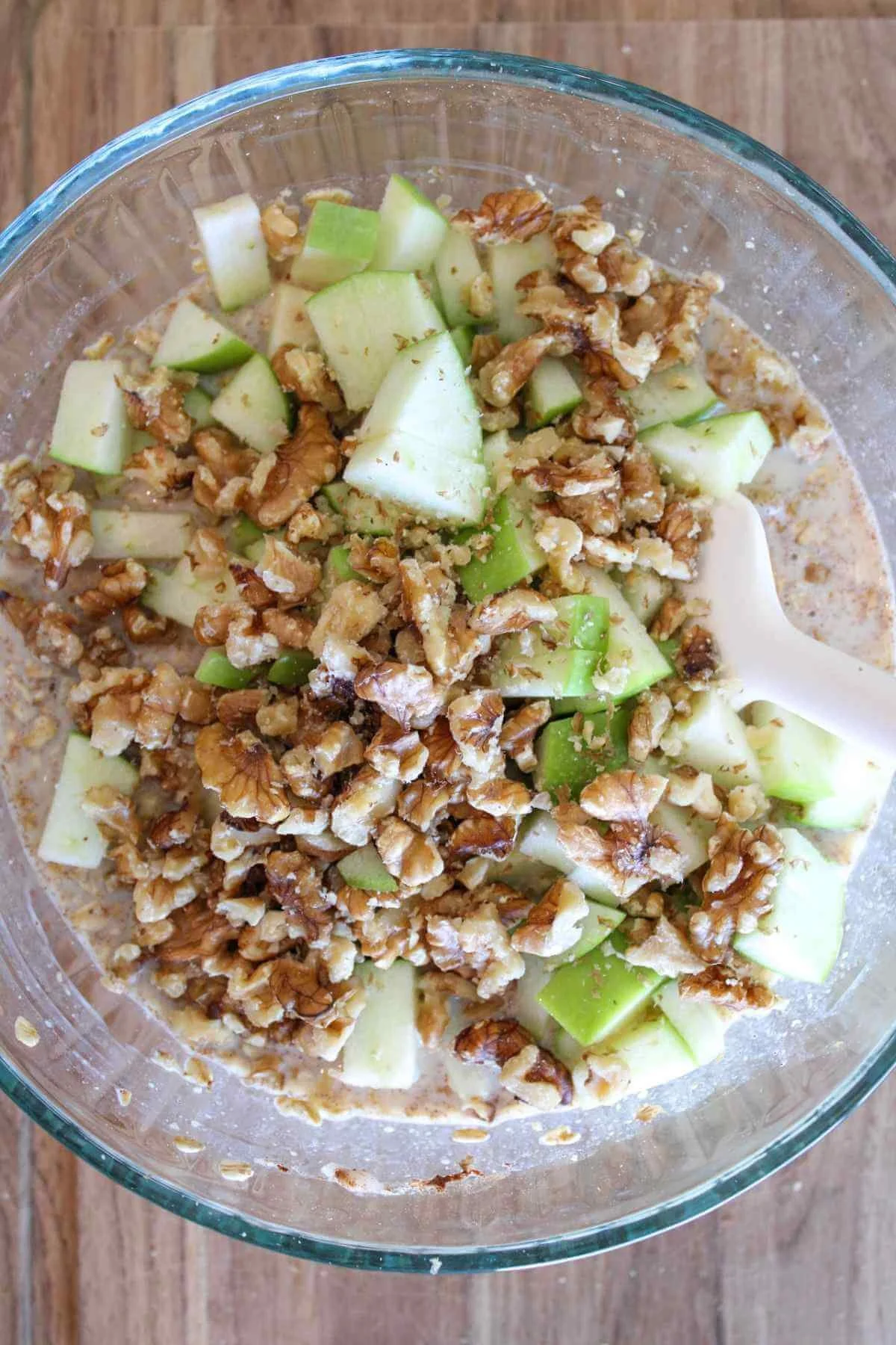 Top-down view of a glass bowl filled with creamy oatmeal, diced green apples, and crunchy walnuts, creating a fresh, wholesome breakfast.