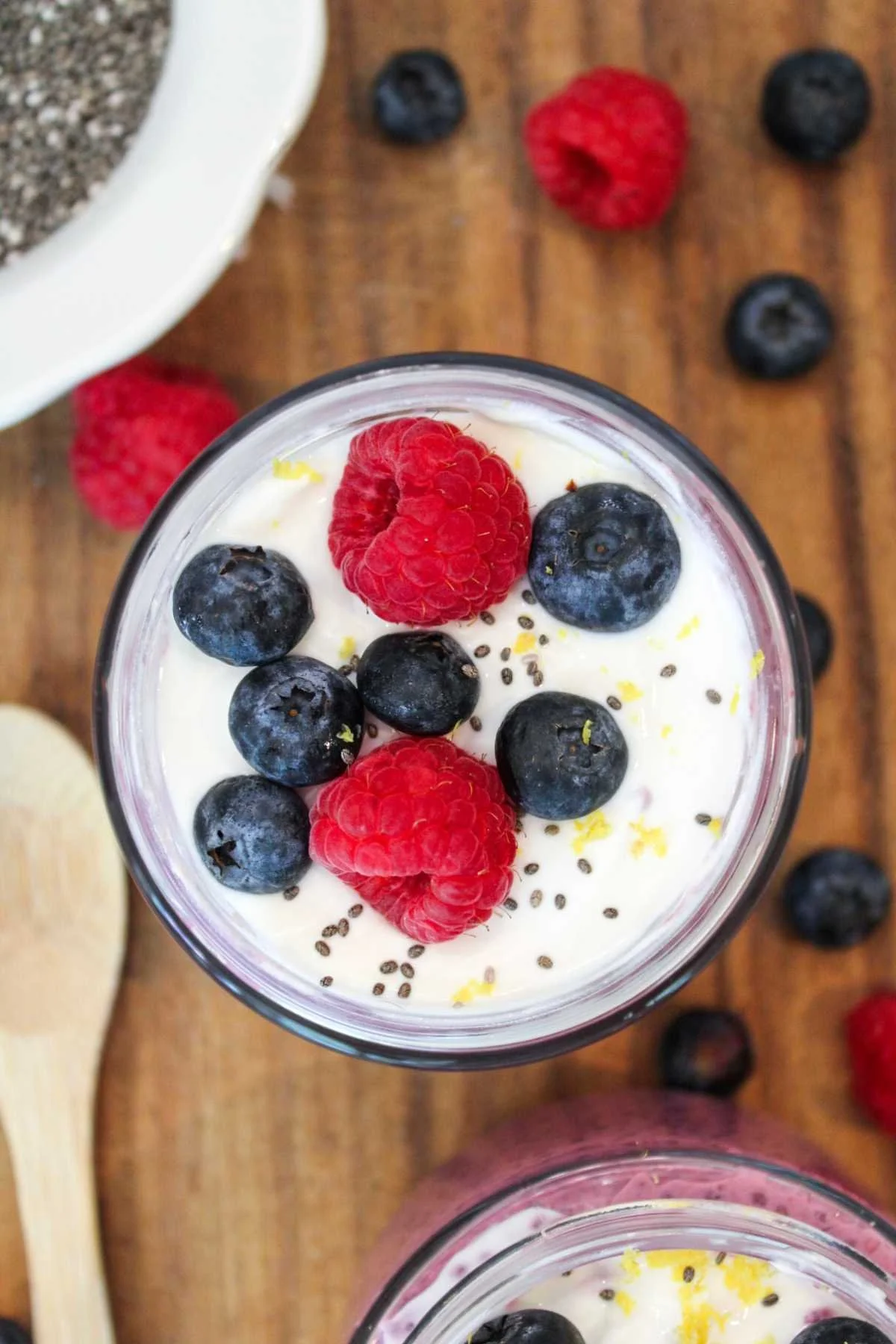 Two jars of berry chia seed pudding served on a wooden cutting board and topped with vanilla greek yogurt and fresh berries.
