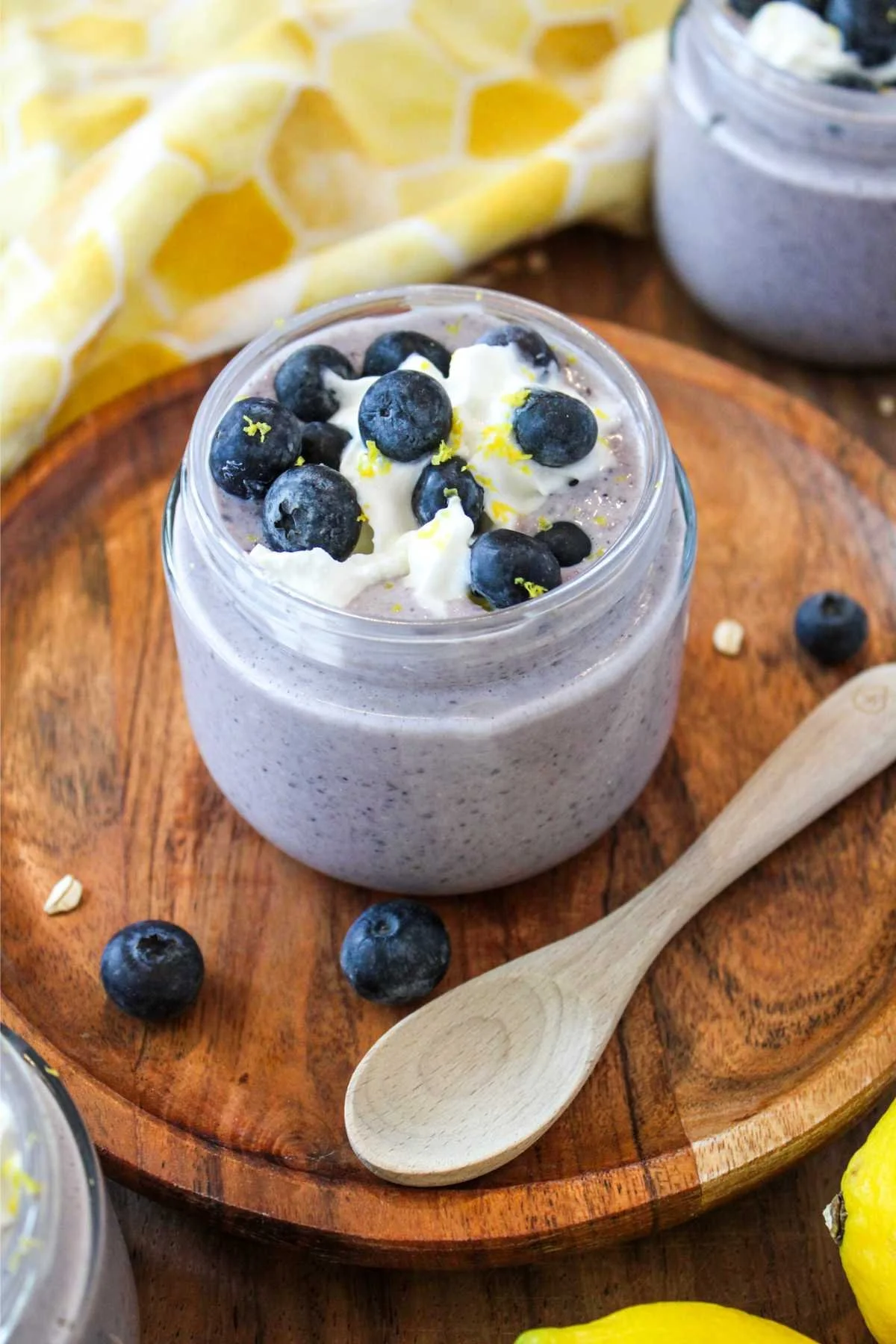 Creamy blueberry overnight oatmeal with whipped cream and fresh blueberries in a jar on a wooden tray, accompanied by a wooden spoon. Bright, inviting feel.