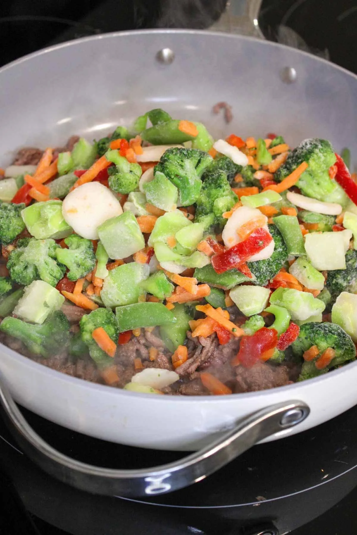 Frozen stir fry vegetables steaming in a pan of browned ground beef to make the base of ground beef lettuce wraps.