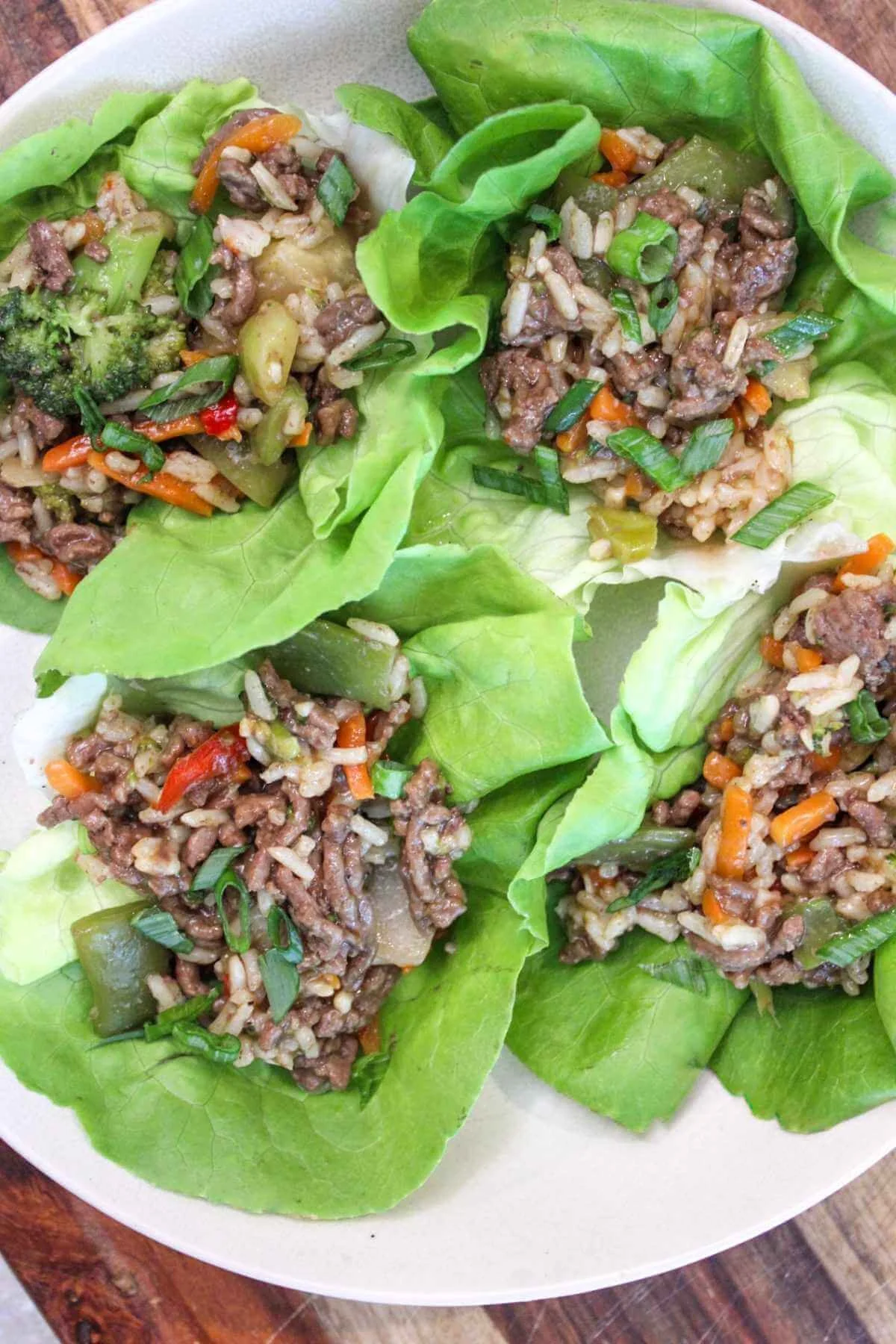 White plate showcasing four ground beef lettuce wraps with low sodium teriyaki sauce and topped with green onion garnish.