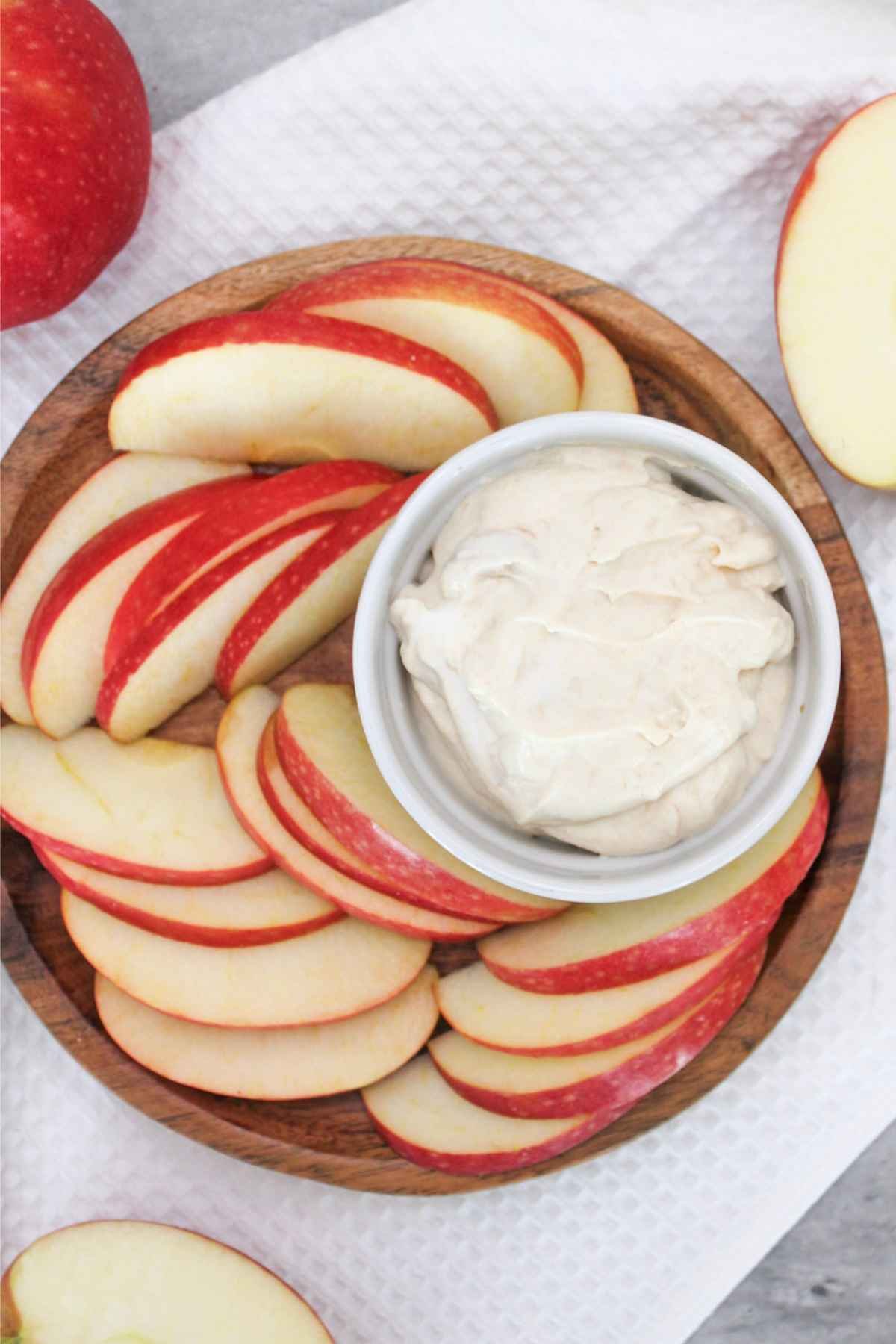 fresh apple slices wrapped around a high protein peanut butter greek yogurt dip and served on a wooden plate for a delicious snack idea.