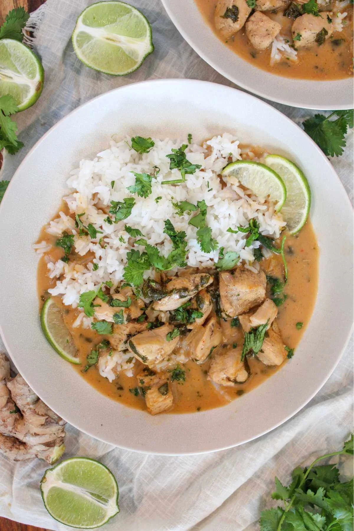 Overhead view of creamy coconut chicken curry with white rice, cilantro, and lime wedges in a bowl, styled on rustic cloth; warm and appetizing.