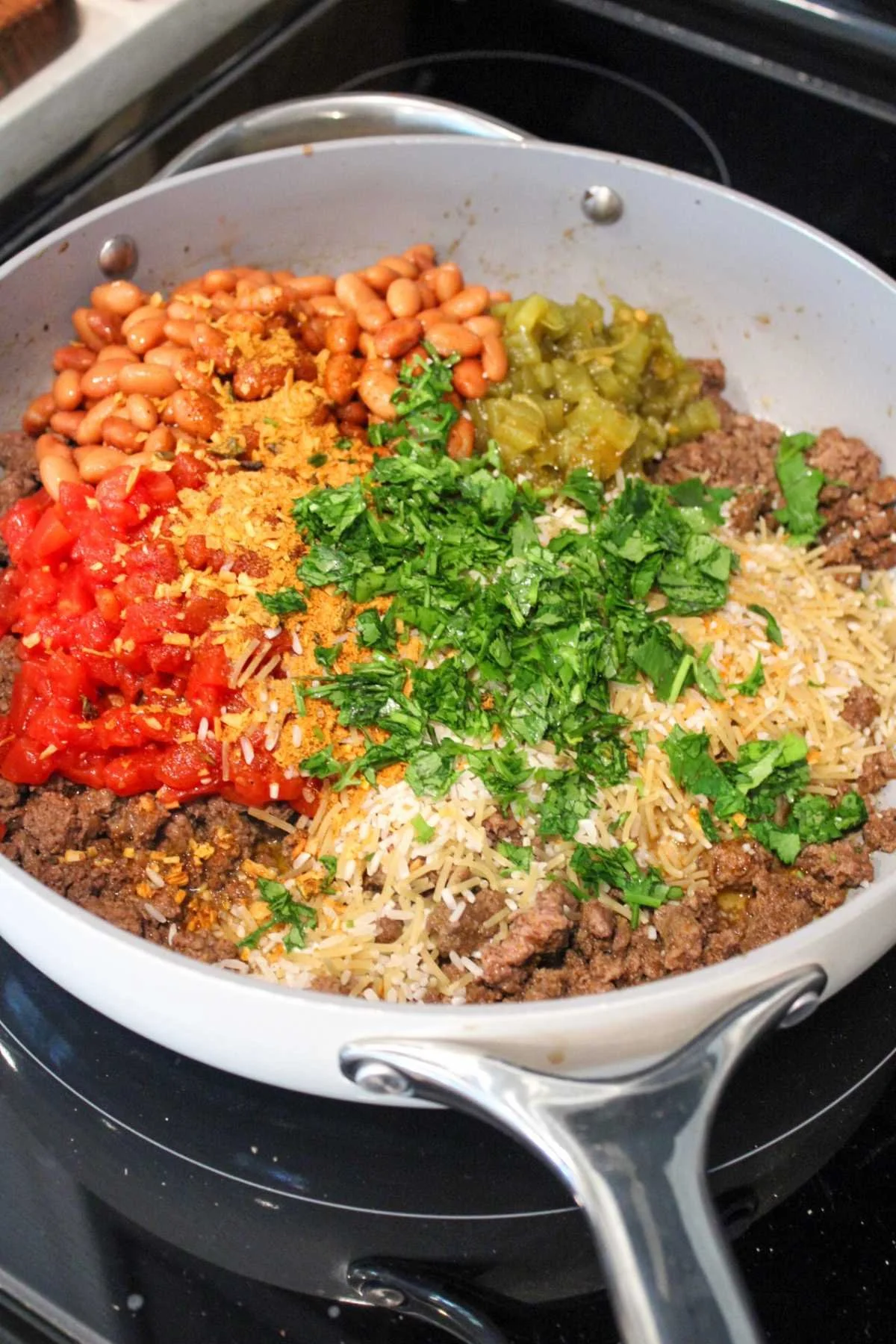 A skillet filled with ground beef, diced tomatoes, pinto beans, chopped green peppers, shredded cheese, and cilantro, creating a colorful, hearty mix.
