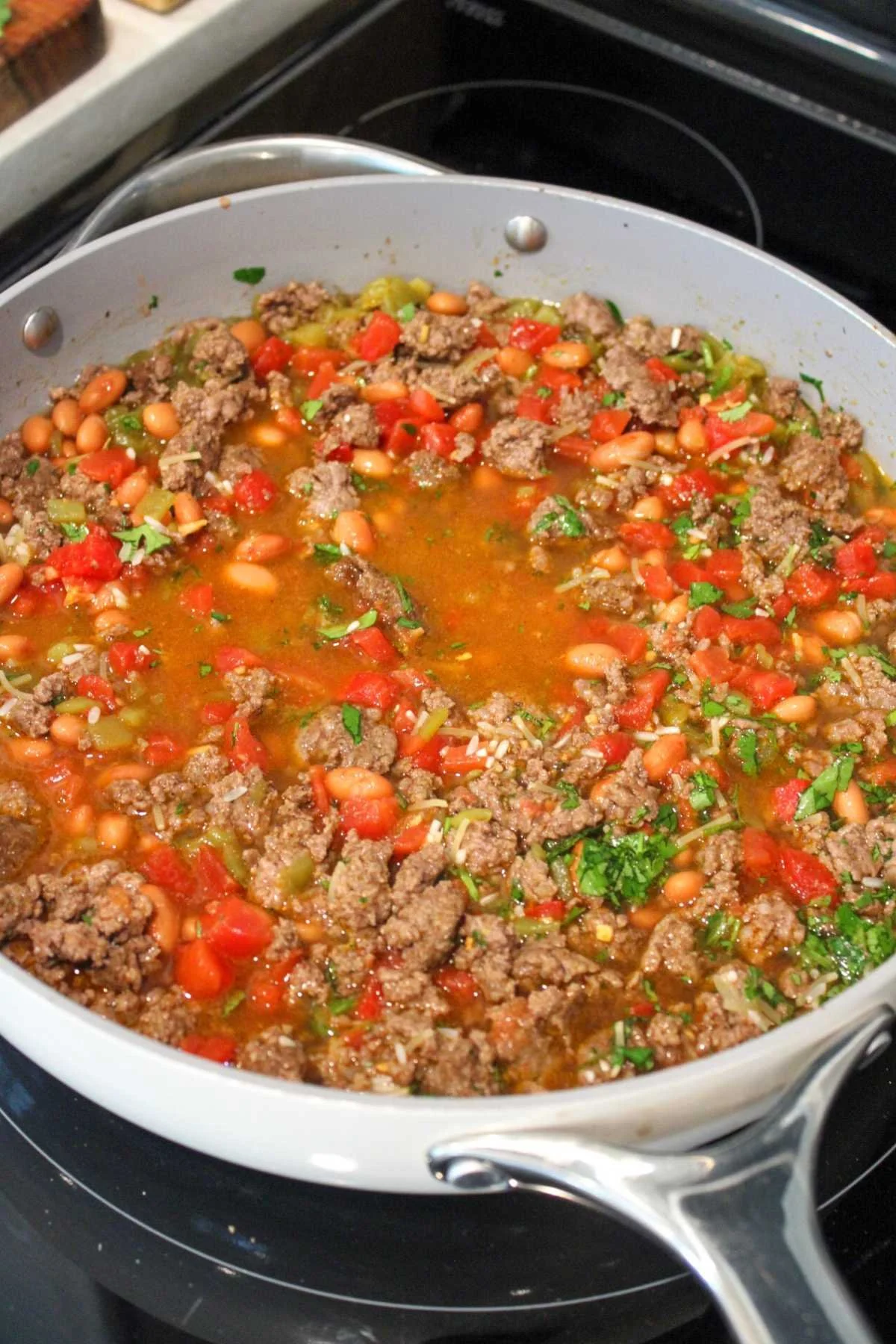 A skillet filled with a colorful chili made of ground beef, beans, tomatoes, and herbs. The dish is simmering, emitting a hearty and savory aroma.
