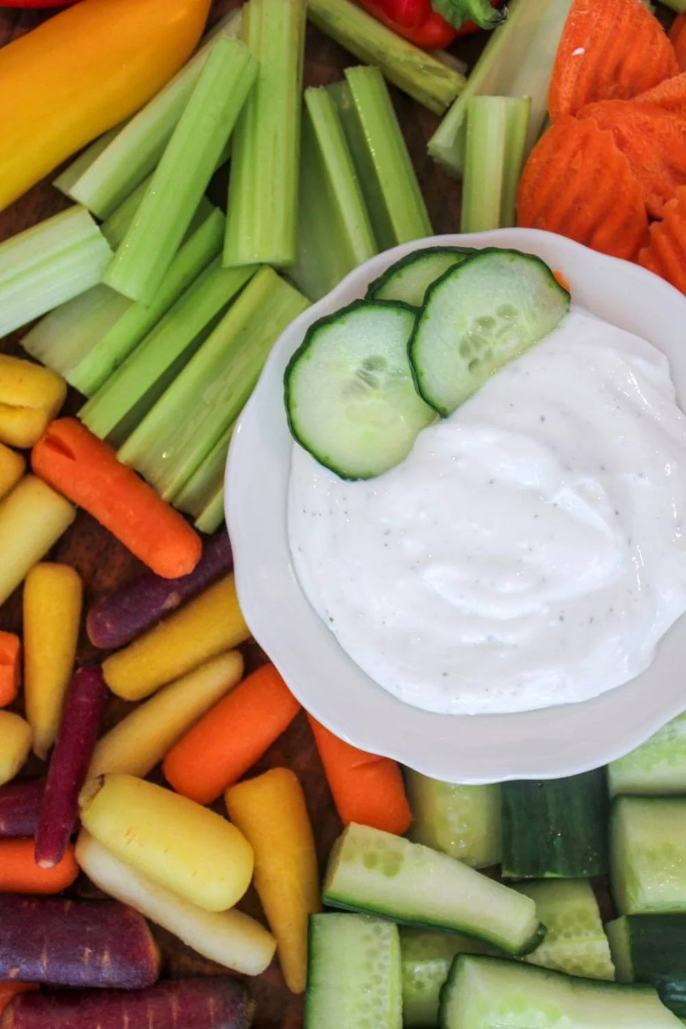 cottage cheese ranch dip served in a small white bowl with cucumber slices as garnish and a background of fresh vegetables to serve with the healthy dip recipe.