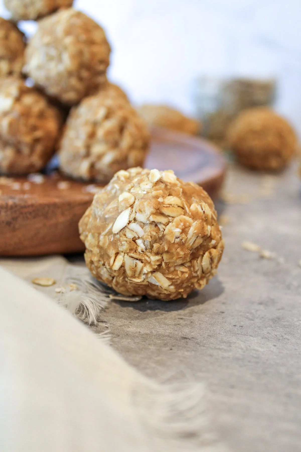 Peanut butter oatmeal ball in front of a wooden plate that is filled with other peanut butter oatmeal balls.