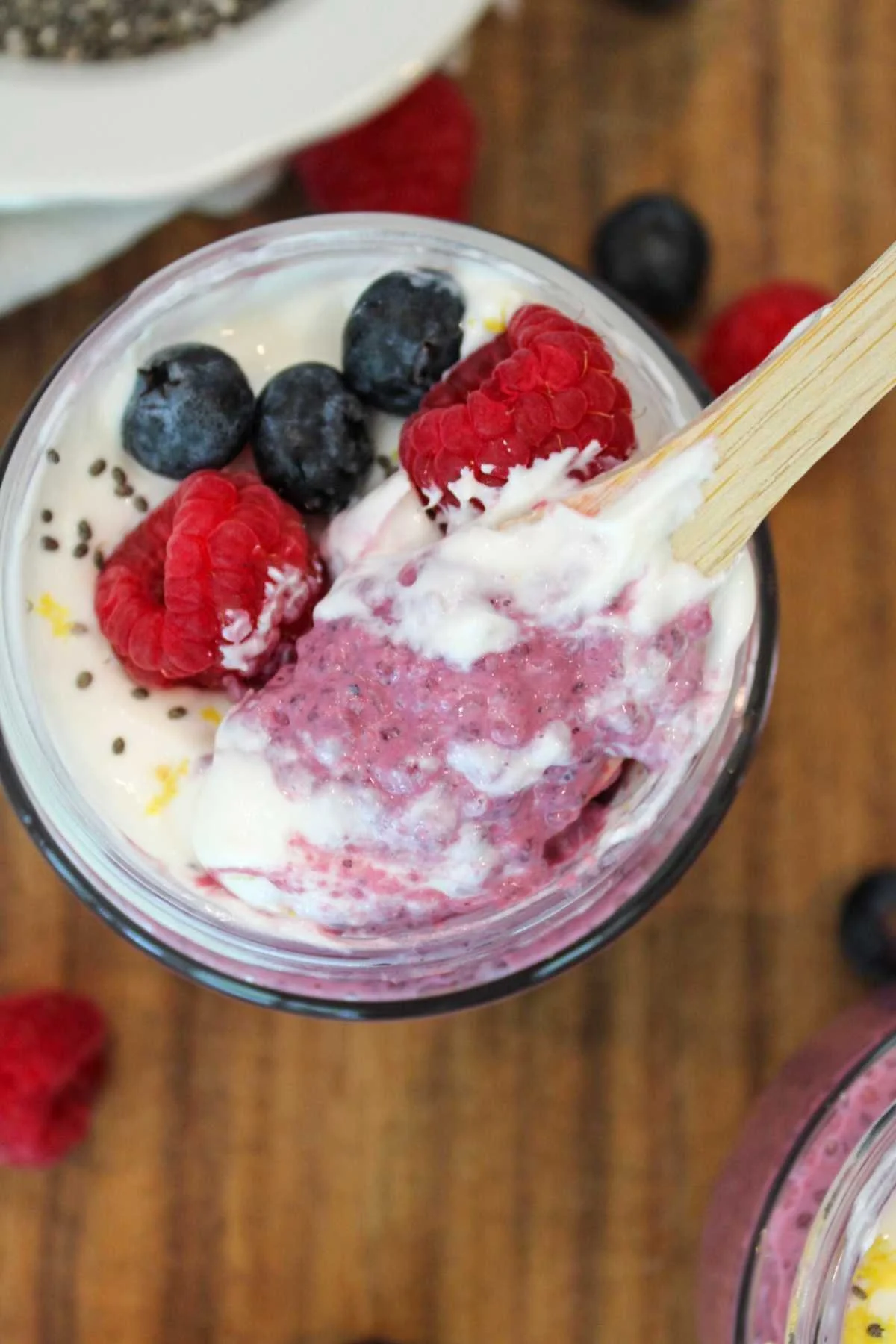 Wooden spoon taking a scoop out of a berry chia pudding recipe with yogurt and fresh berries on top.