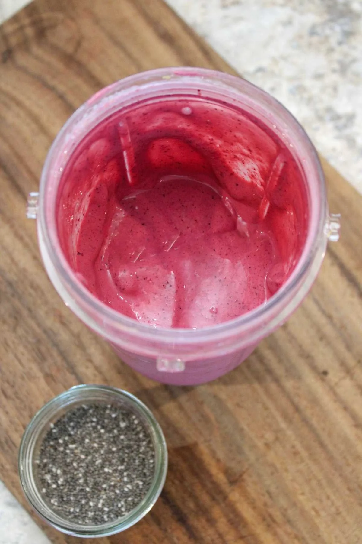 Blended cup with a purple smoothie mixture and served on a wooden cutting board.