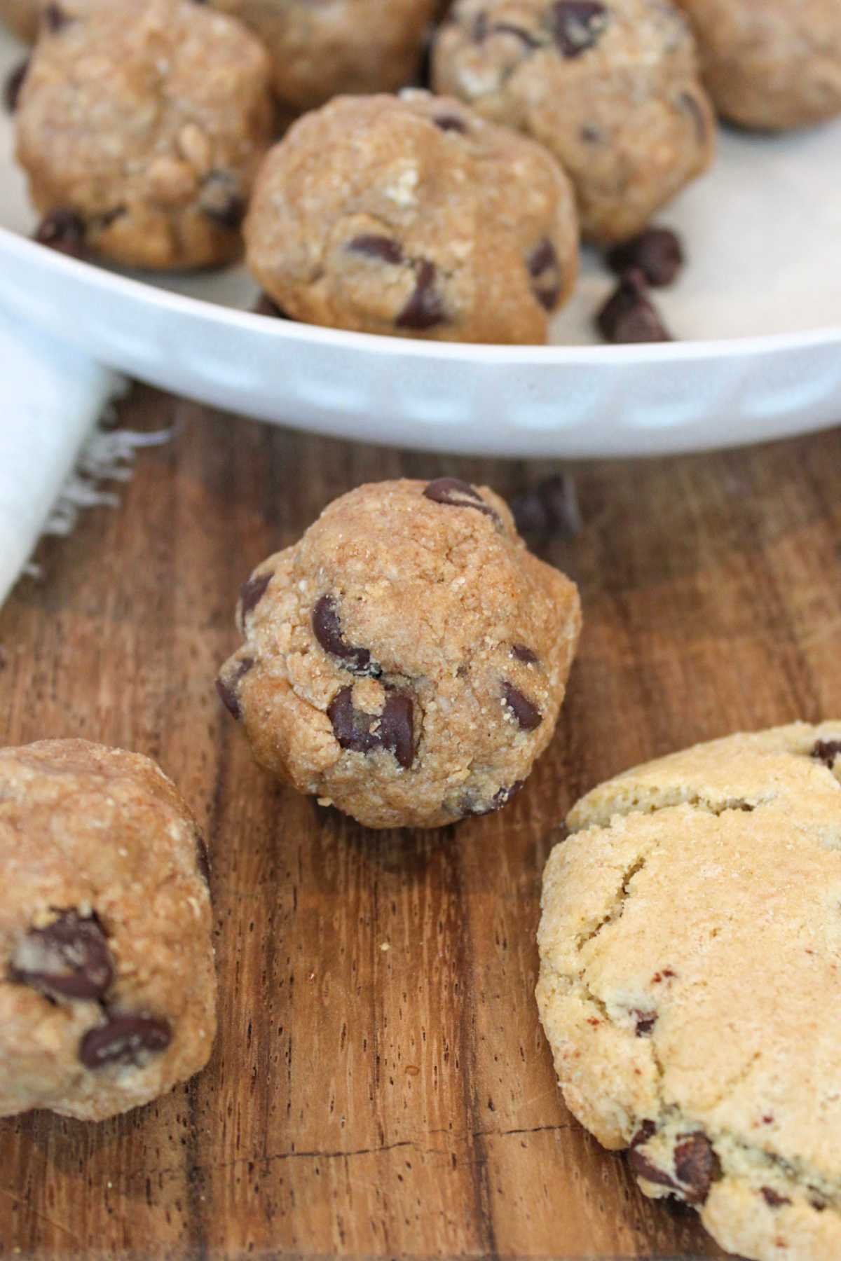 Plate of round chocolate chip cookies on wooden surface, with some cookies scattered in foreground. The scene evokes a warm, homemade feel.