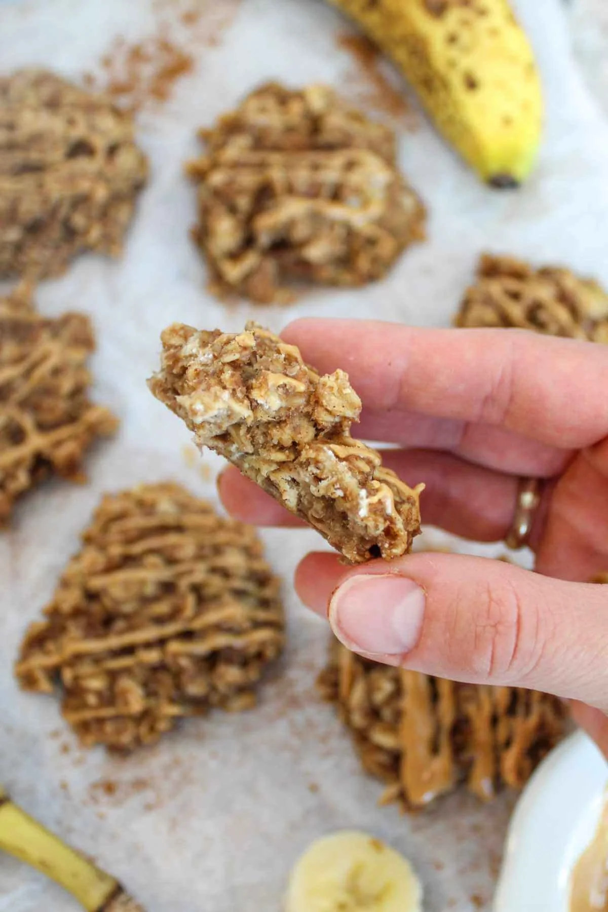 A hand holding a peanut butter oatmeal cookie with a background of other peanut butter oatmeal cookies on parchment paper.
