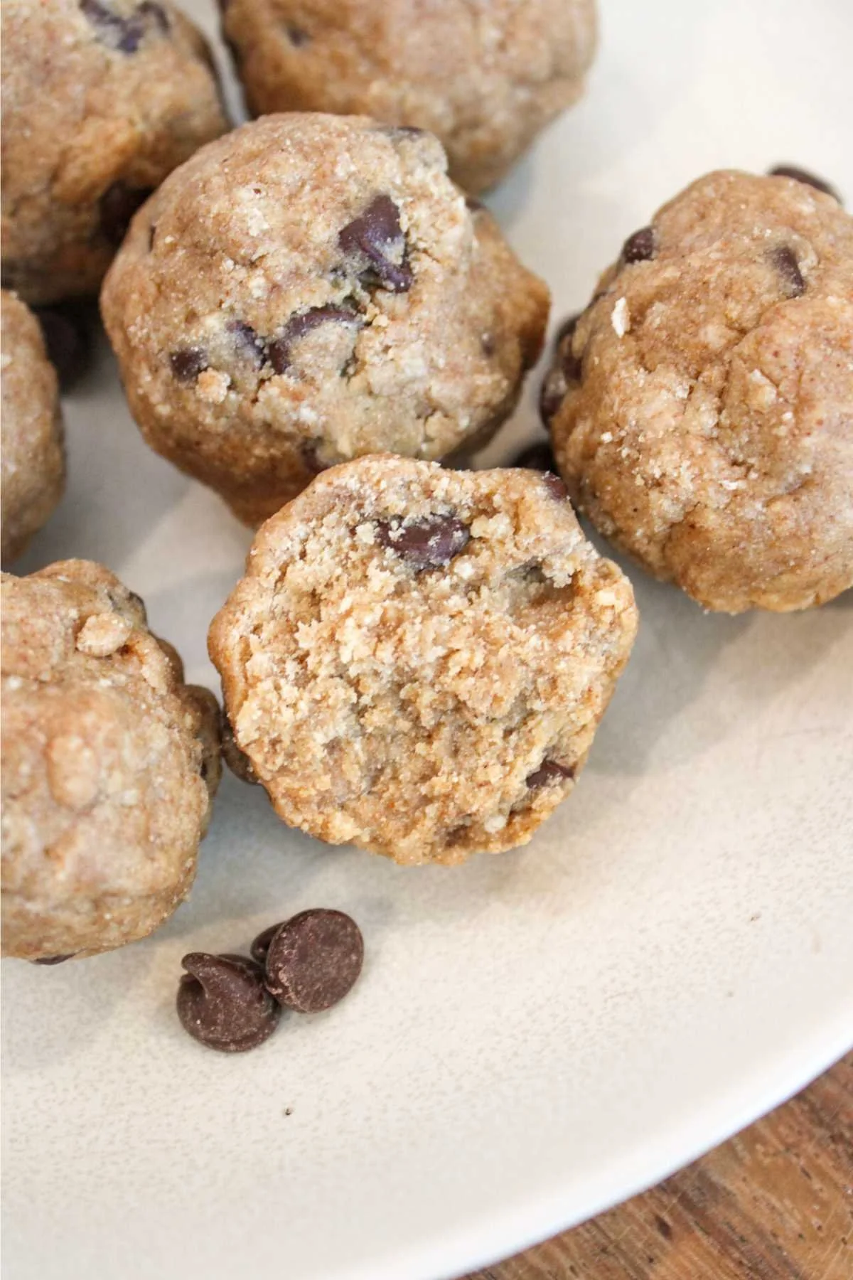 Homemade chocolate chip protein cookie dough balls on a white plate, with a few chocolate chips on the side, conveying a warm, inviting feel.