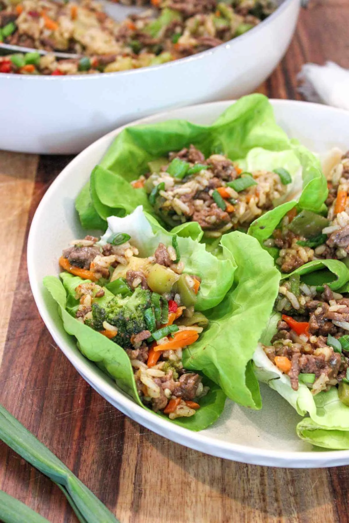 a white plate of teriyaki ground beef lettuce wraps with the ground beef mixture in the background and served on a wooden platter.
