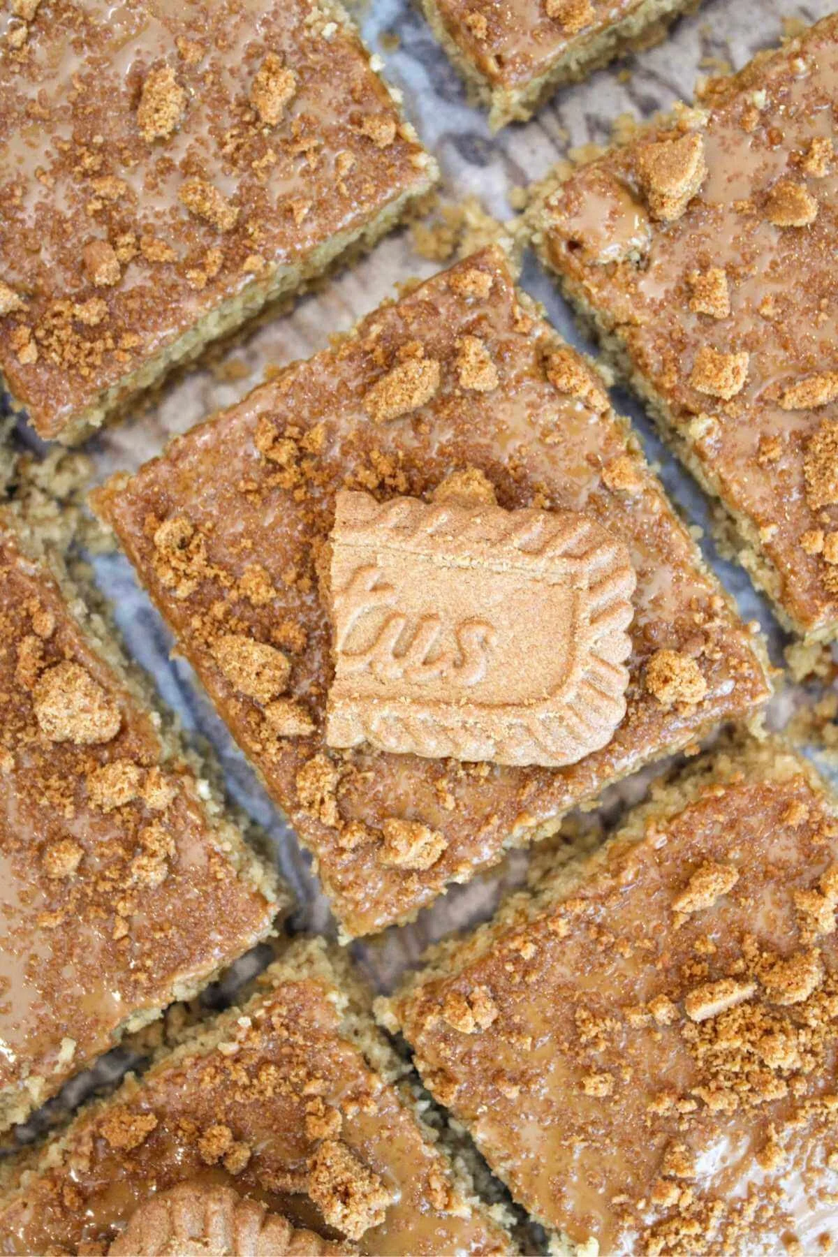 Close-up of golden-brown dessert bars topped with crunchy crumbs, arranged on parchment; the center bar features a stamped wafer cookie.