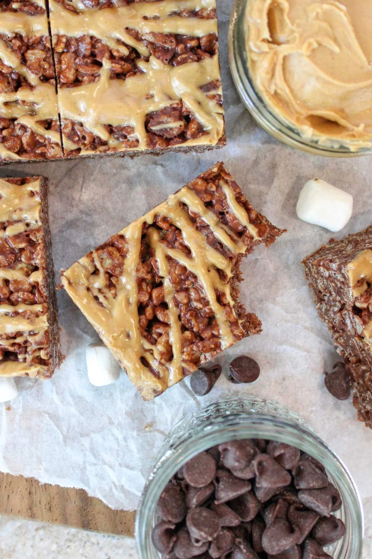 peanut butter and chocolate Rice Krispie treats drizzled in peanut butter and served on parchment paper with marshmallows and chocolate chips.