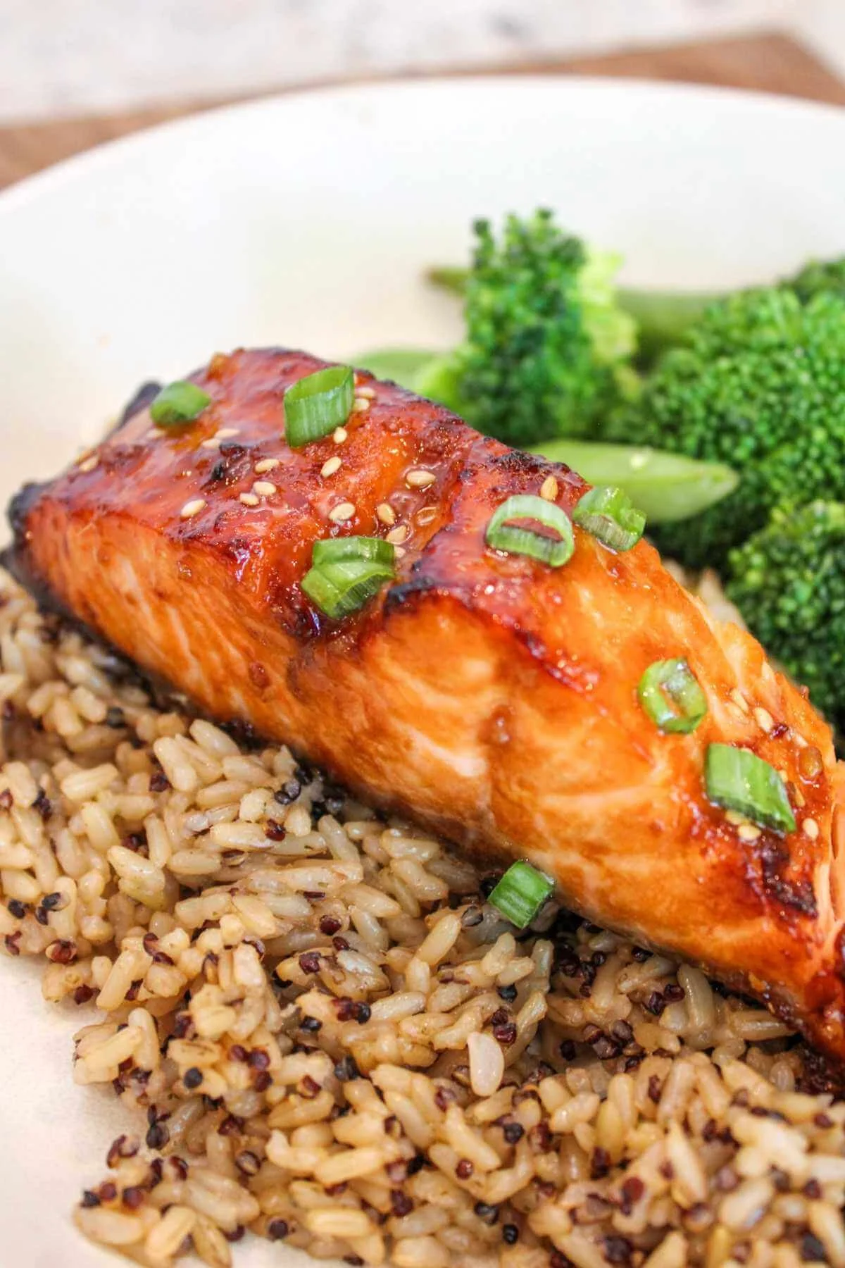 air fryer teriyaki salmon topped with green onions and served over a bed of brown rice with a side of steamed broccoli.