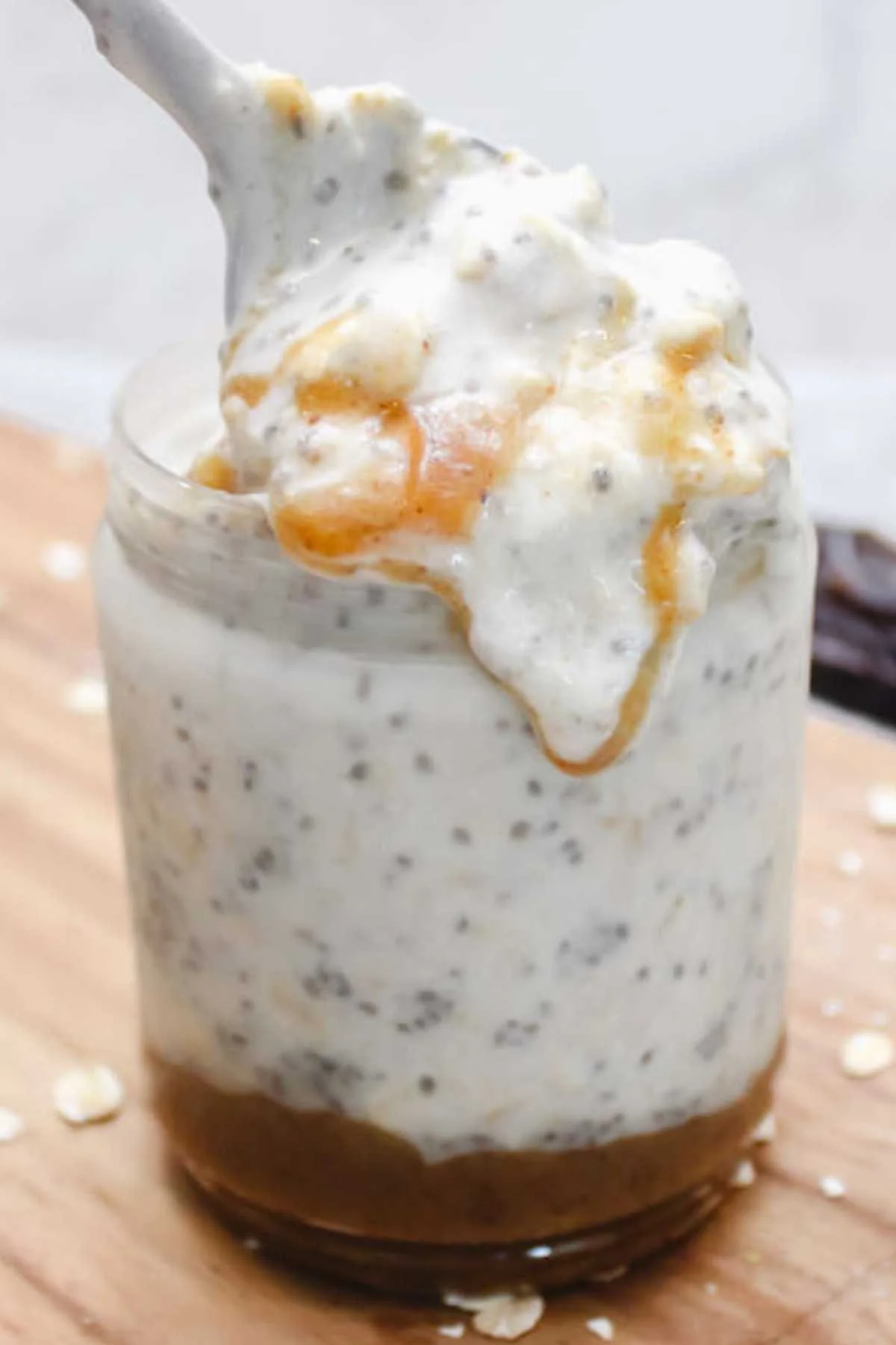 A glass jar holds creamy chia pudding with visible seeds, topped with caramel. A spoon lifts a portion, creating a tempting and indulgent look.