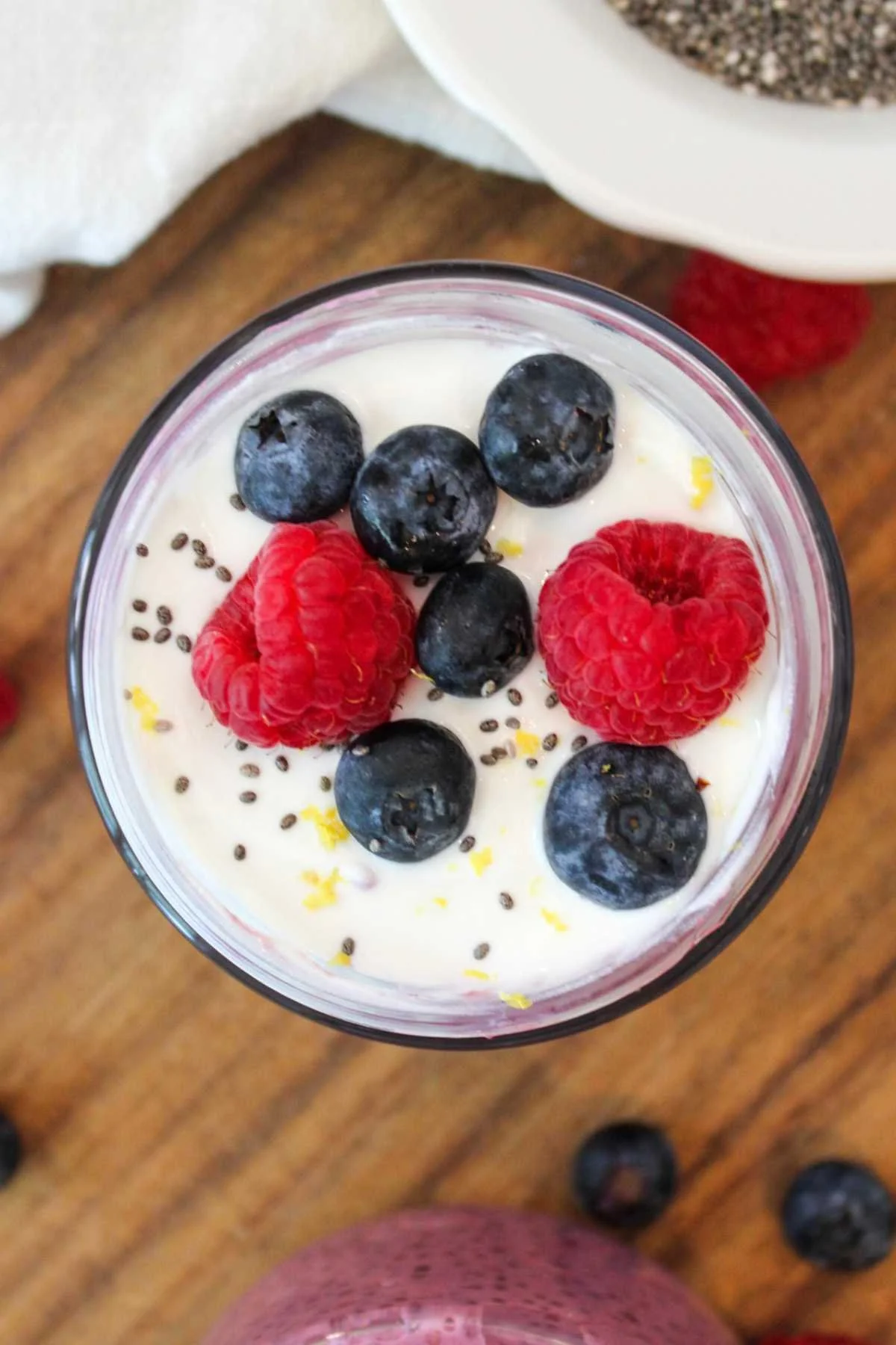 overhead image of berry chia seed pudding topped with fresh berries, vanilla greek yogurt, and lemon zest served on a wooden cutting board.