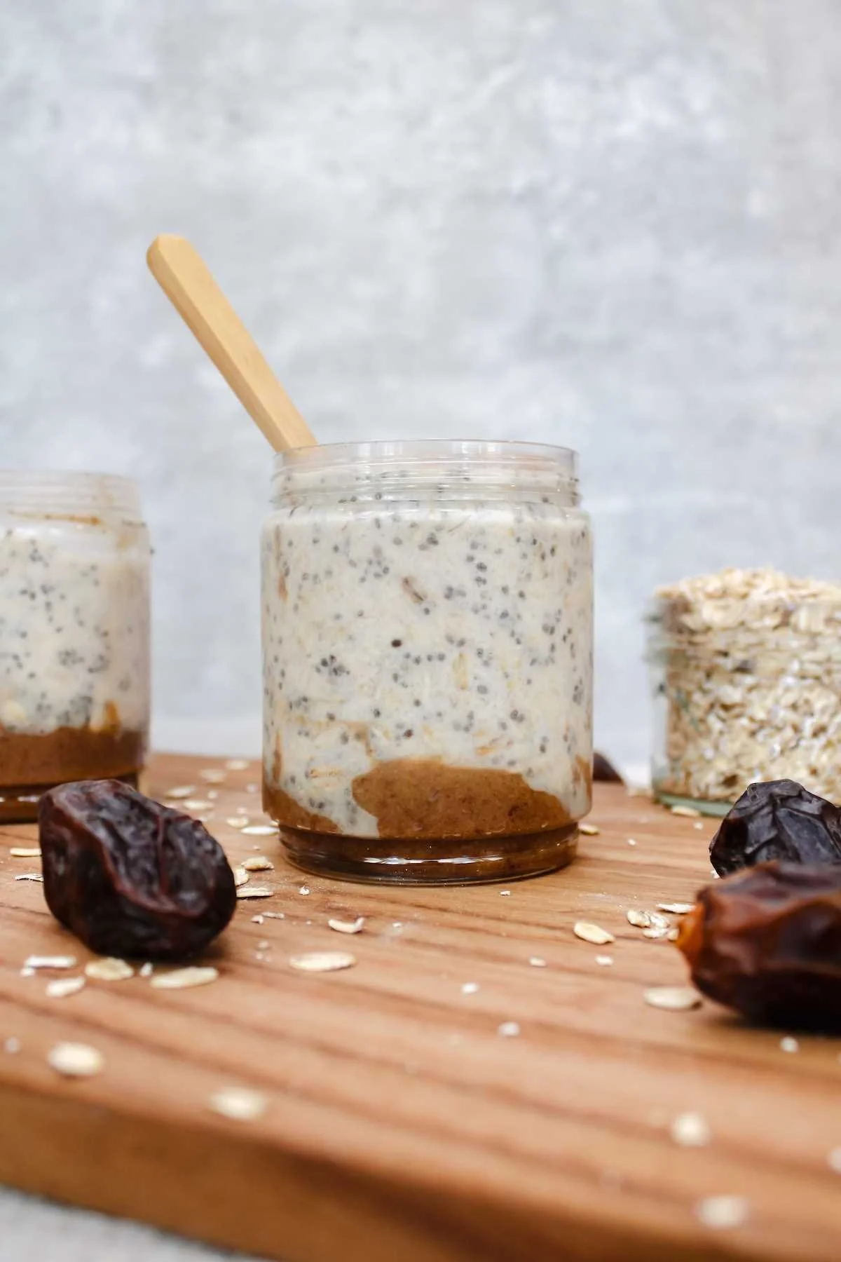 A jar filled with creamy overnight oats, chia seeds, and a layer of date paste sits on a wooden board, surrounded by dates and oats, emanating a wholesome vibe.