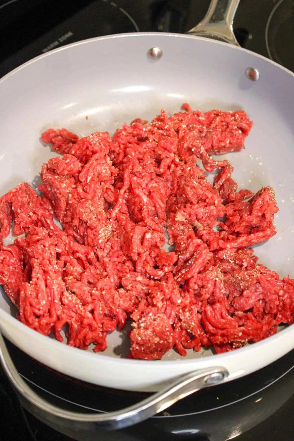 Raw ground beef cooking in a large ceramic pan.