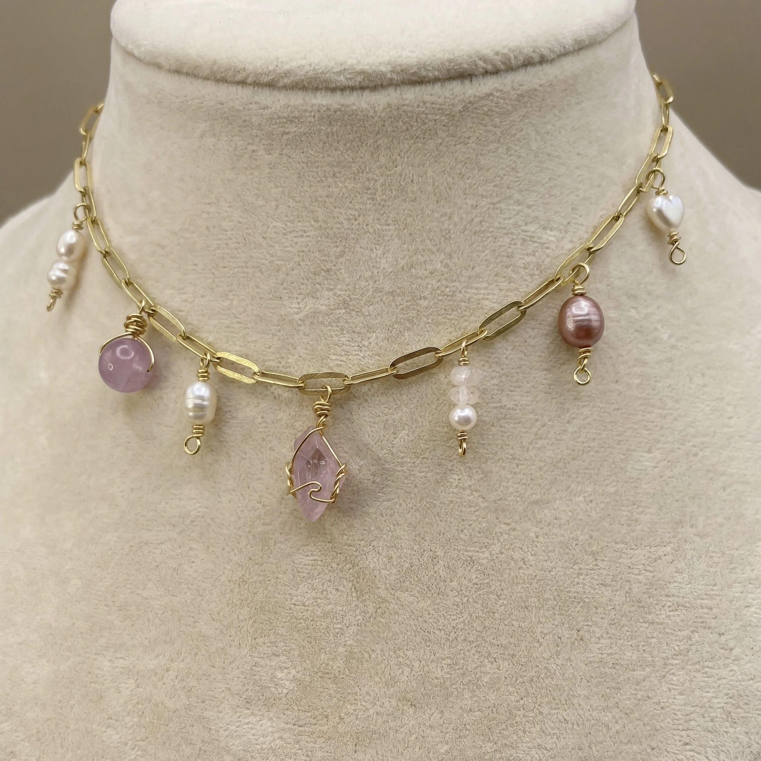 Close-up of a person wearing layered gold necklaces with various pendants, including a pearl, gemstone, and bead, over a white top.