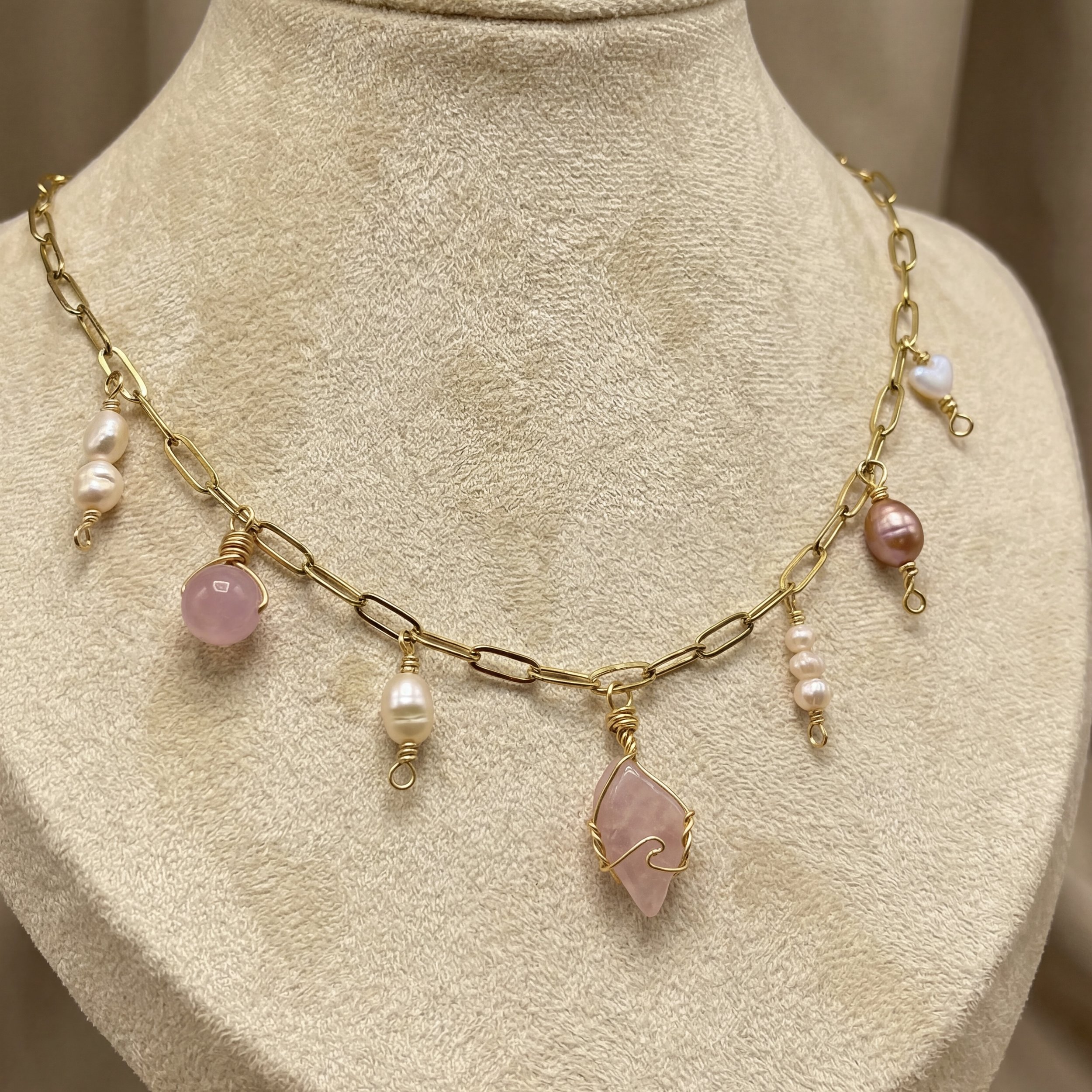 Close-up of a person wearing layered gold necklaces with various pendants, including a pearl, gemstone, and bead, over a white top.