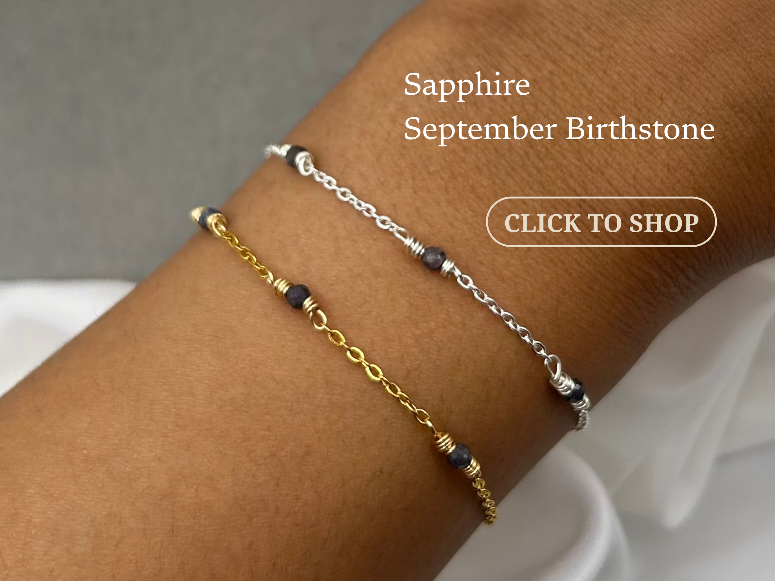Two bracelets on a person's wrist, one silver and one gold, featuring small dark beads, with text indicating the silver bracelet is sapphire and September birthstone.