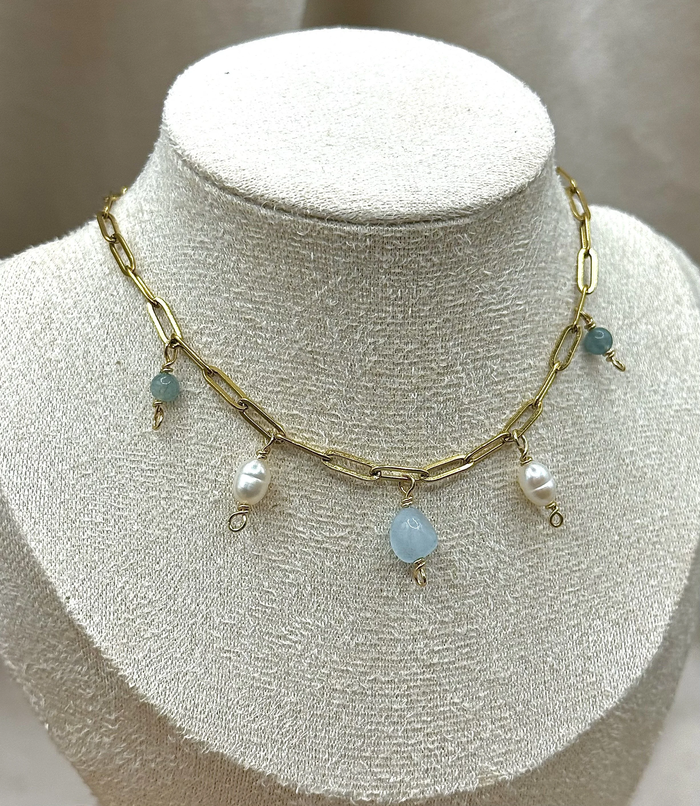 Gold chain necklace with blue and white beads and pearls displayed on a beige jewelry stand.