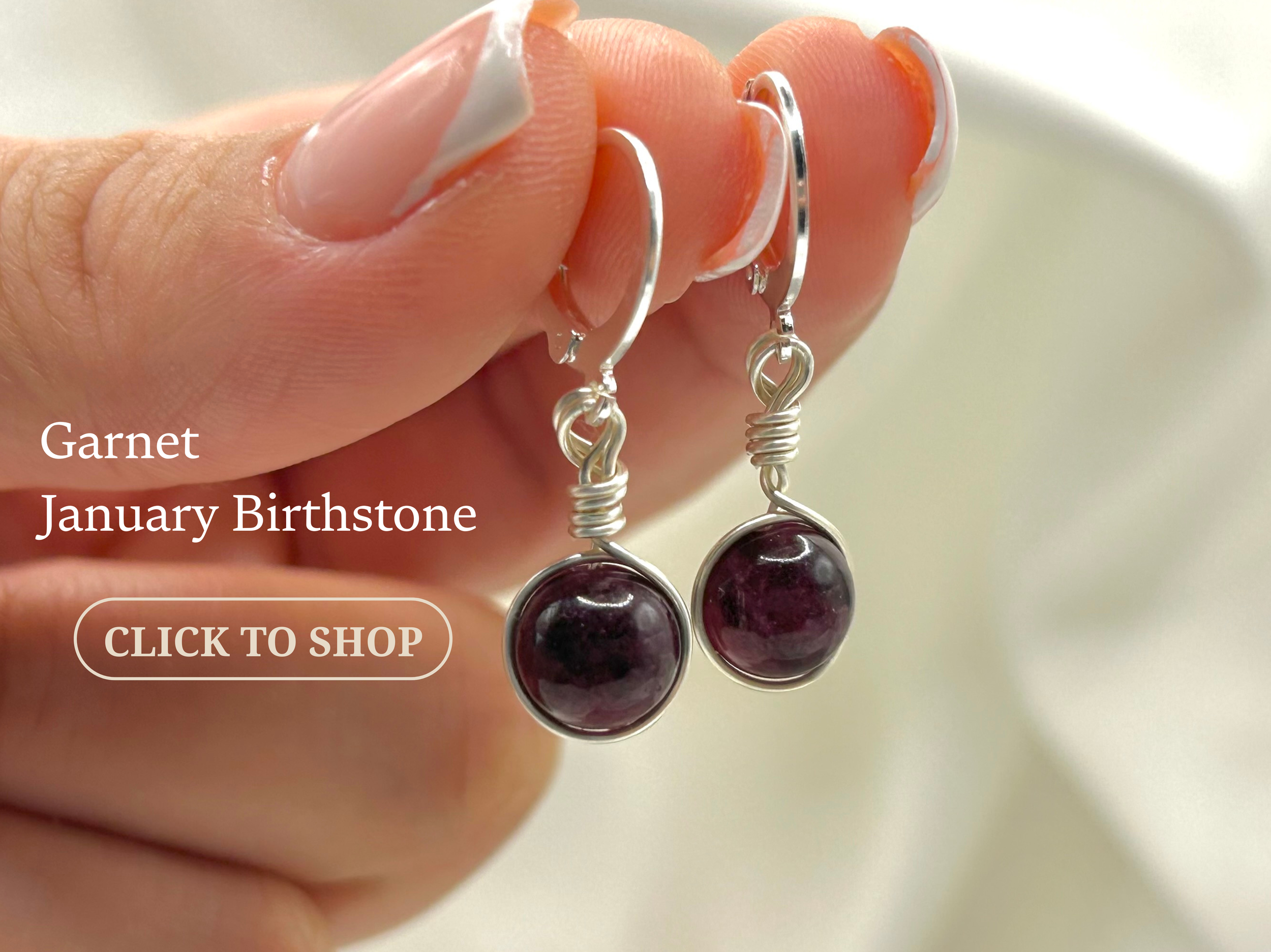 Silver earrings with round dark purple gemstone charms held between fingers.