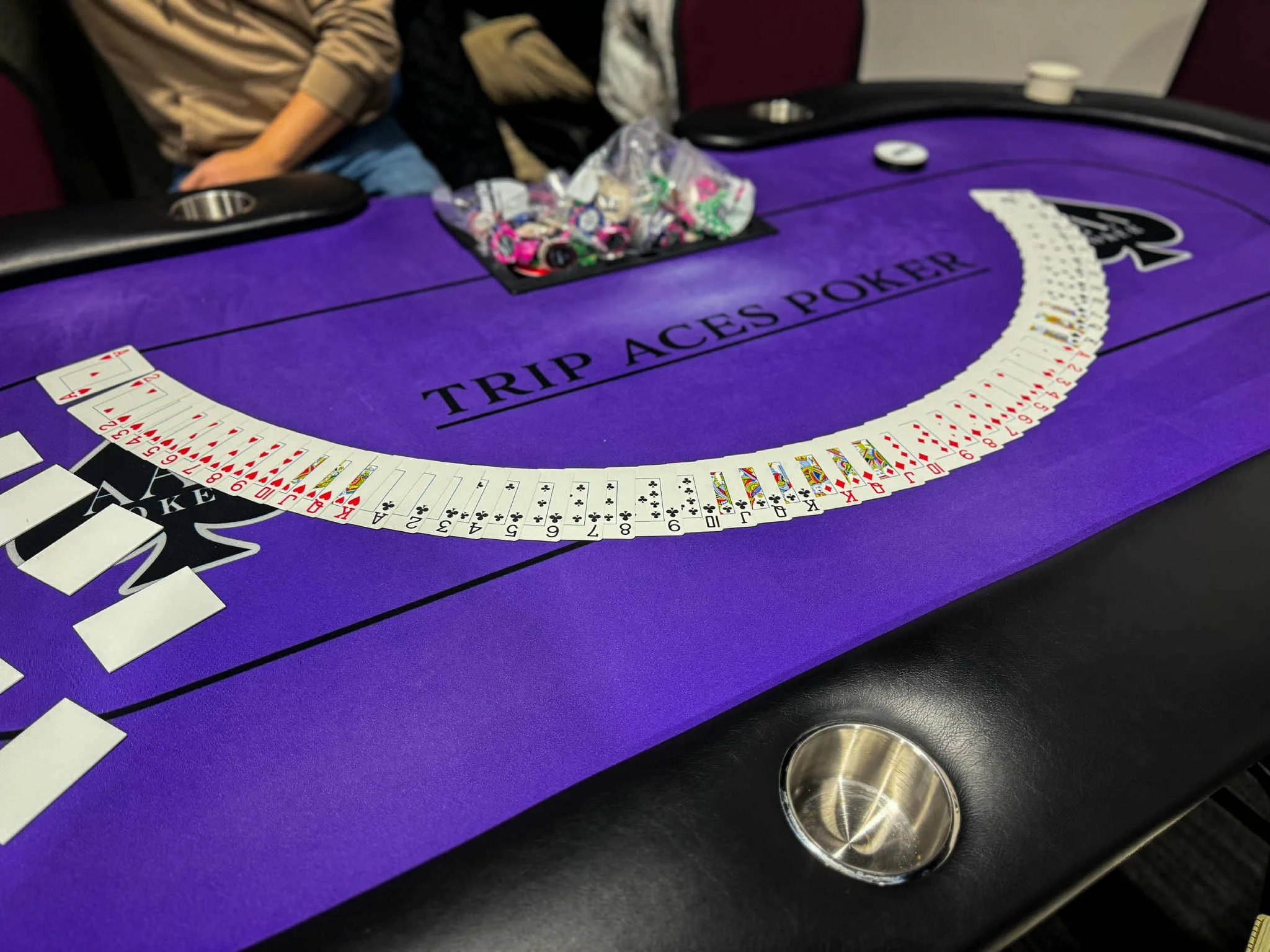 A purple casino table with a semicircular arrangement of playing cards, a pile of poker chips, and a few scattered chips and a coffee cup.