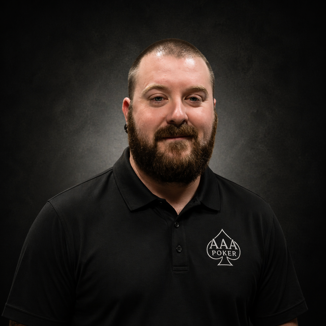 A man with a beard and short hair wearing a black polo shirt with an AAA Poker logo, smiling against a plain dark background.