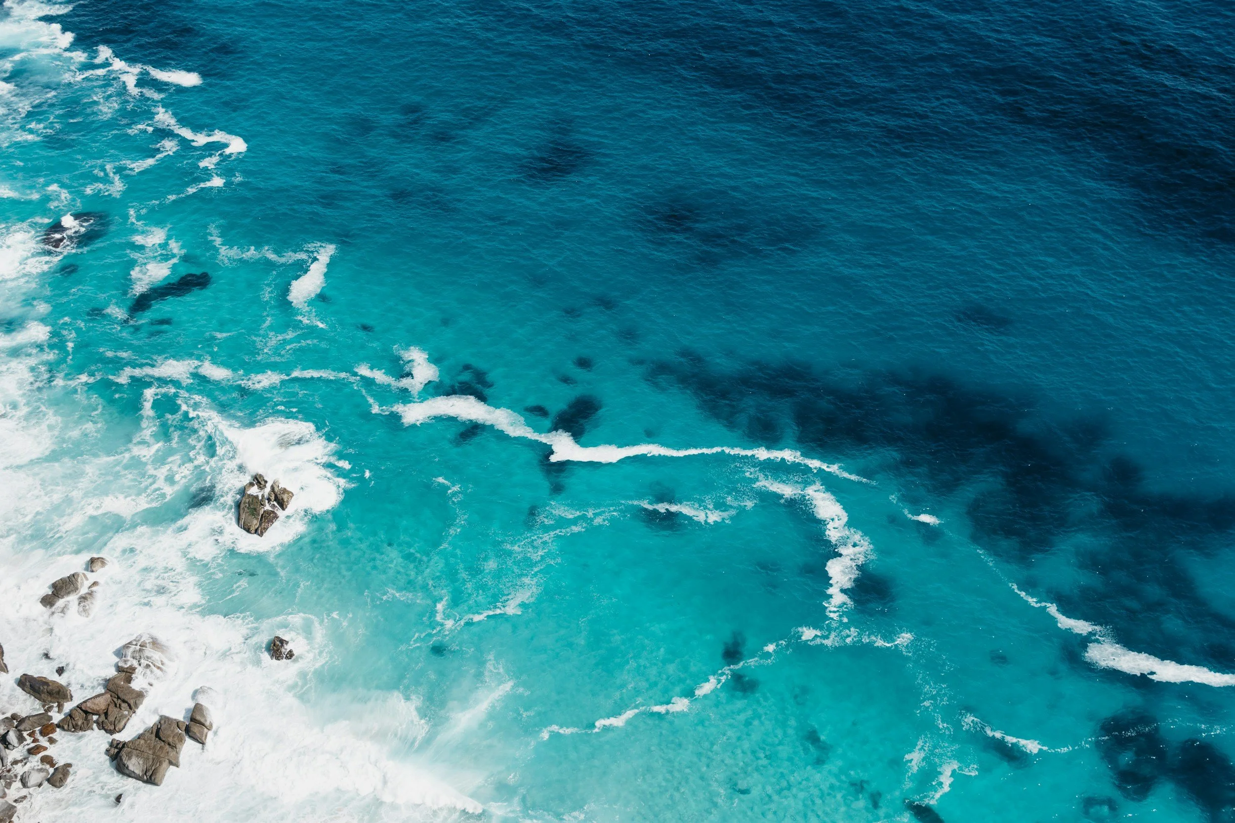 Aerial view of the ocean with waves and rocks along the shoreline.