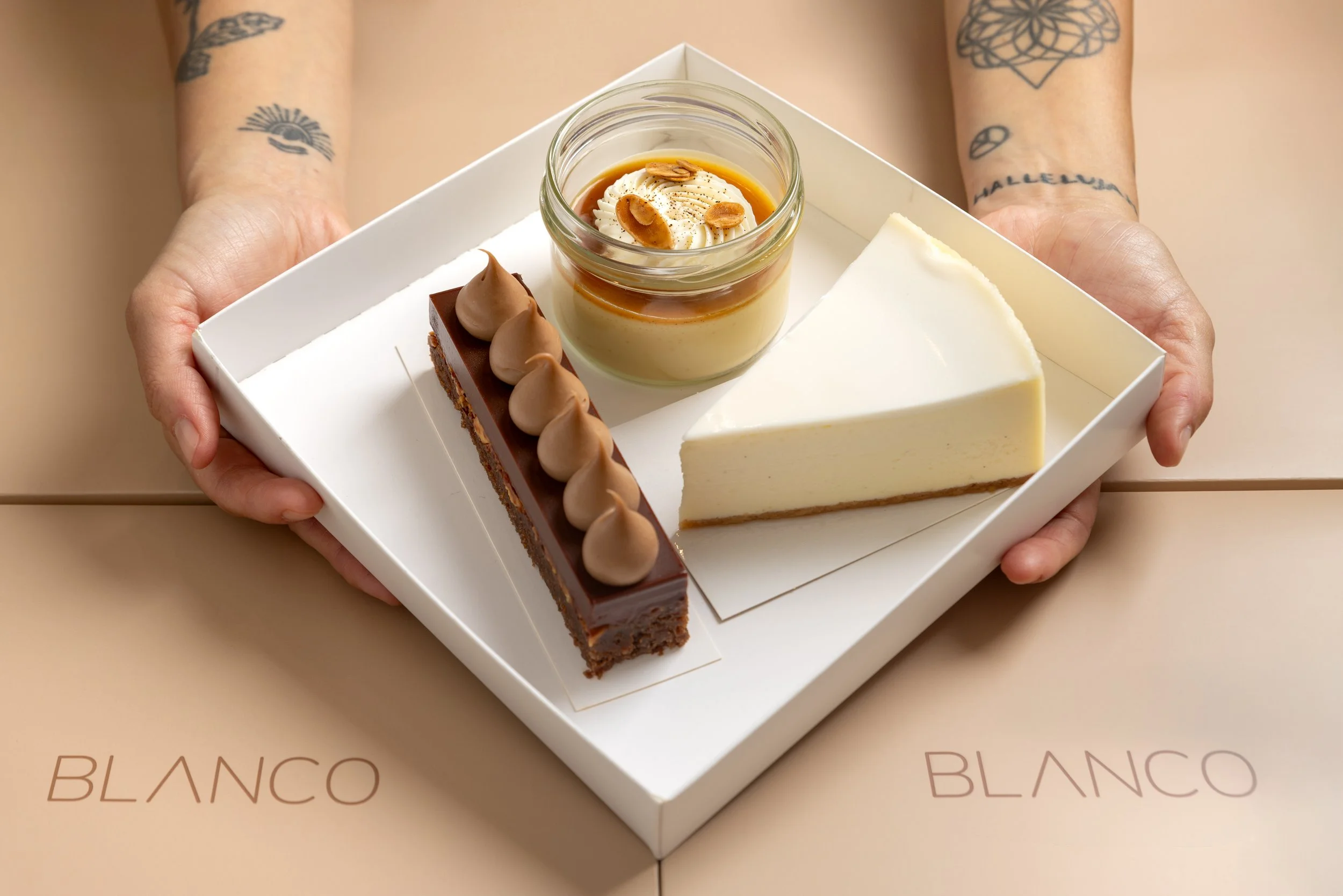 Person holding a white tray with three different slices of cheesecake and a small jar of caramel pudding