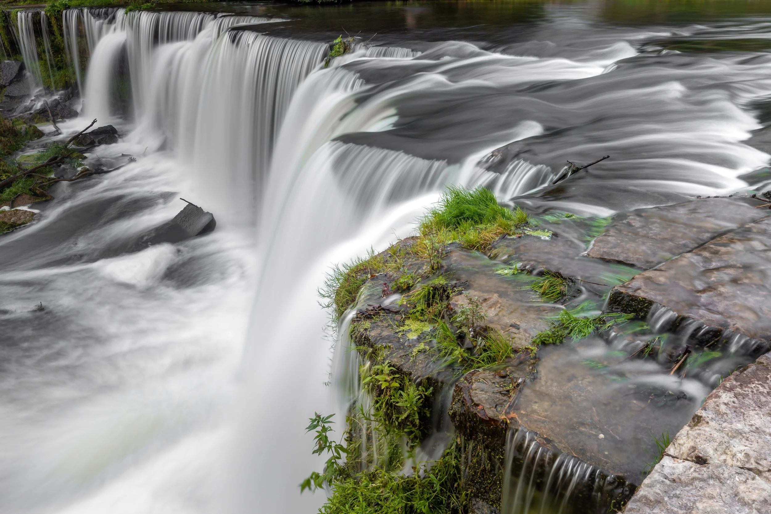 Water cascading over rocks and a small patch of grass at a waterfall.