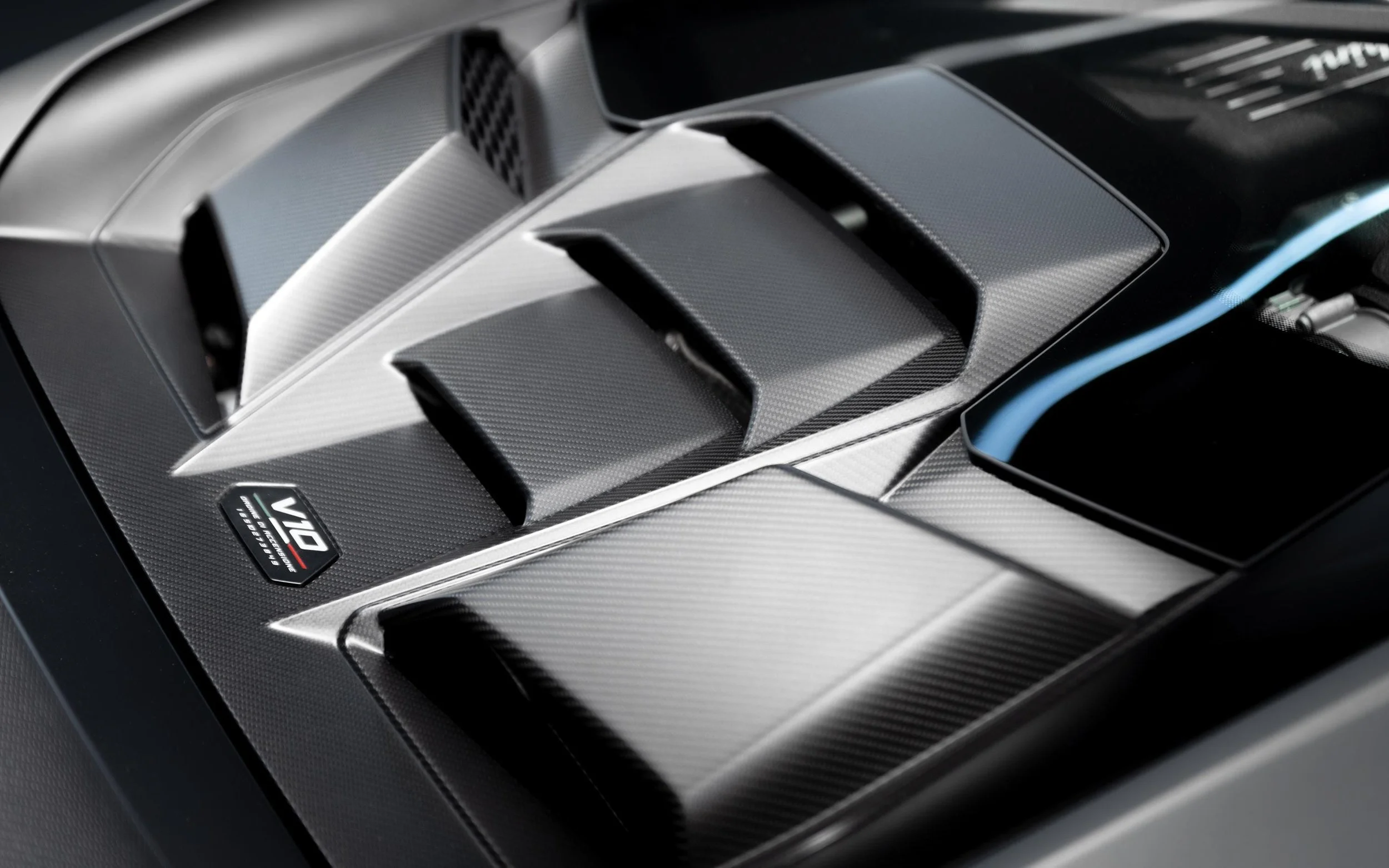 Close-up of a car engine with carbon fiber components and a V10 badge.
