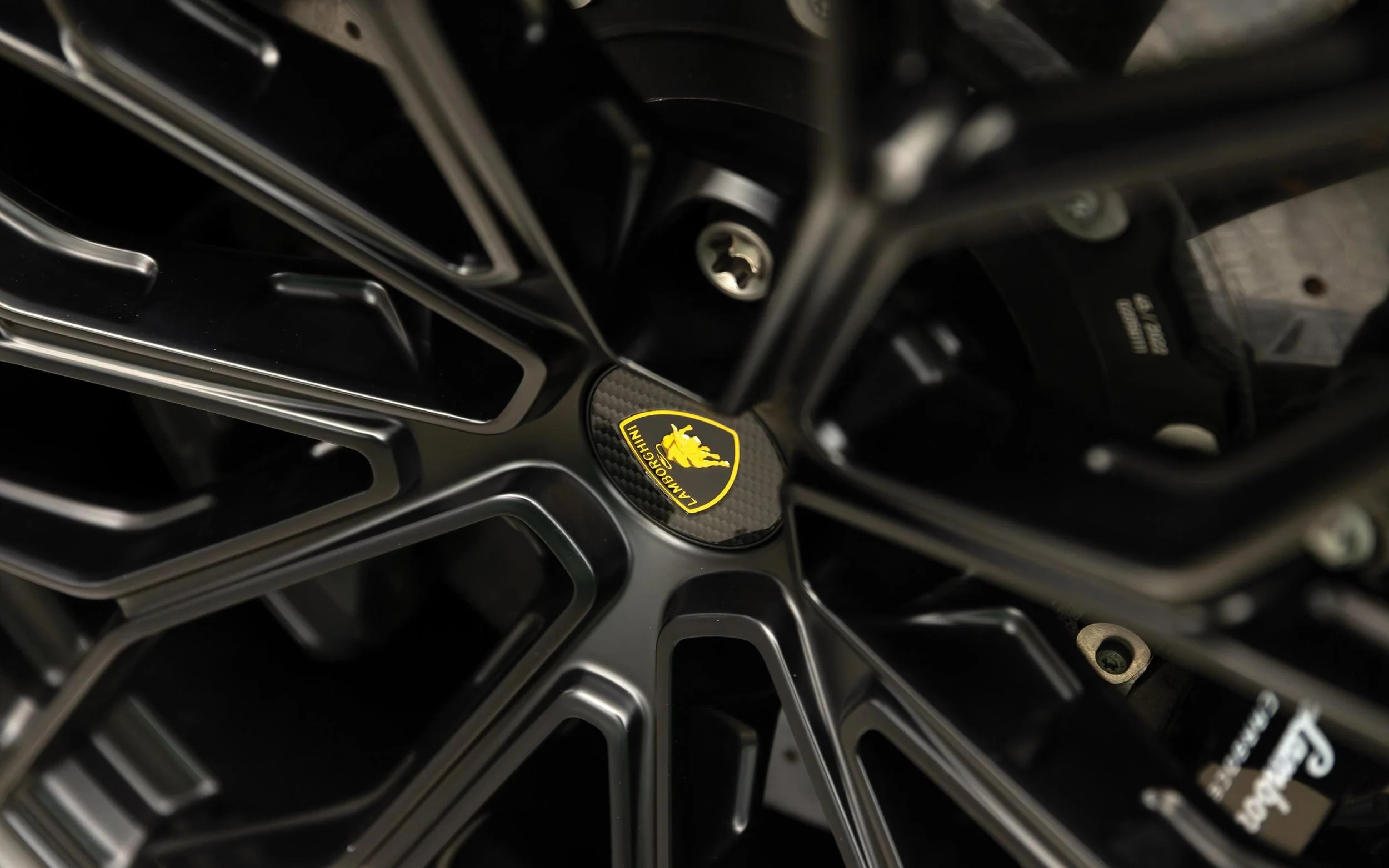 Close-up of a Lamborghini wheel with a black and yellow Lamborghini logo in the center.