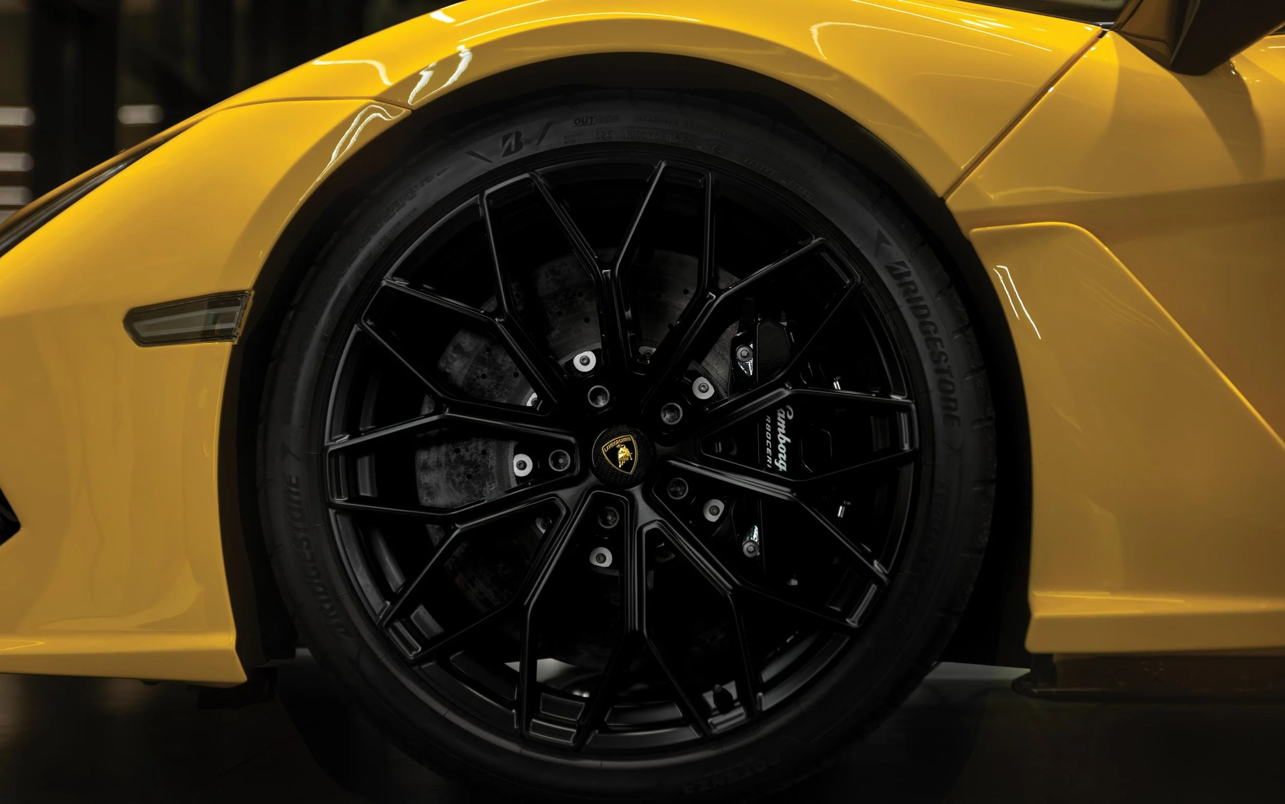 Close-up of a yellow sports car with a black wheel, showing Lamborghini logo and Bridgestone tire.
