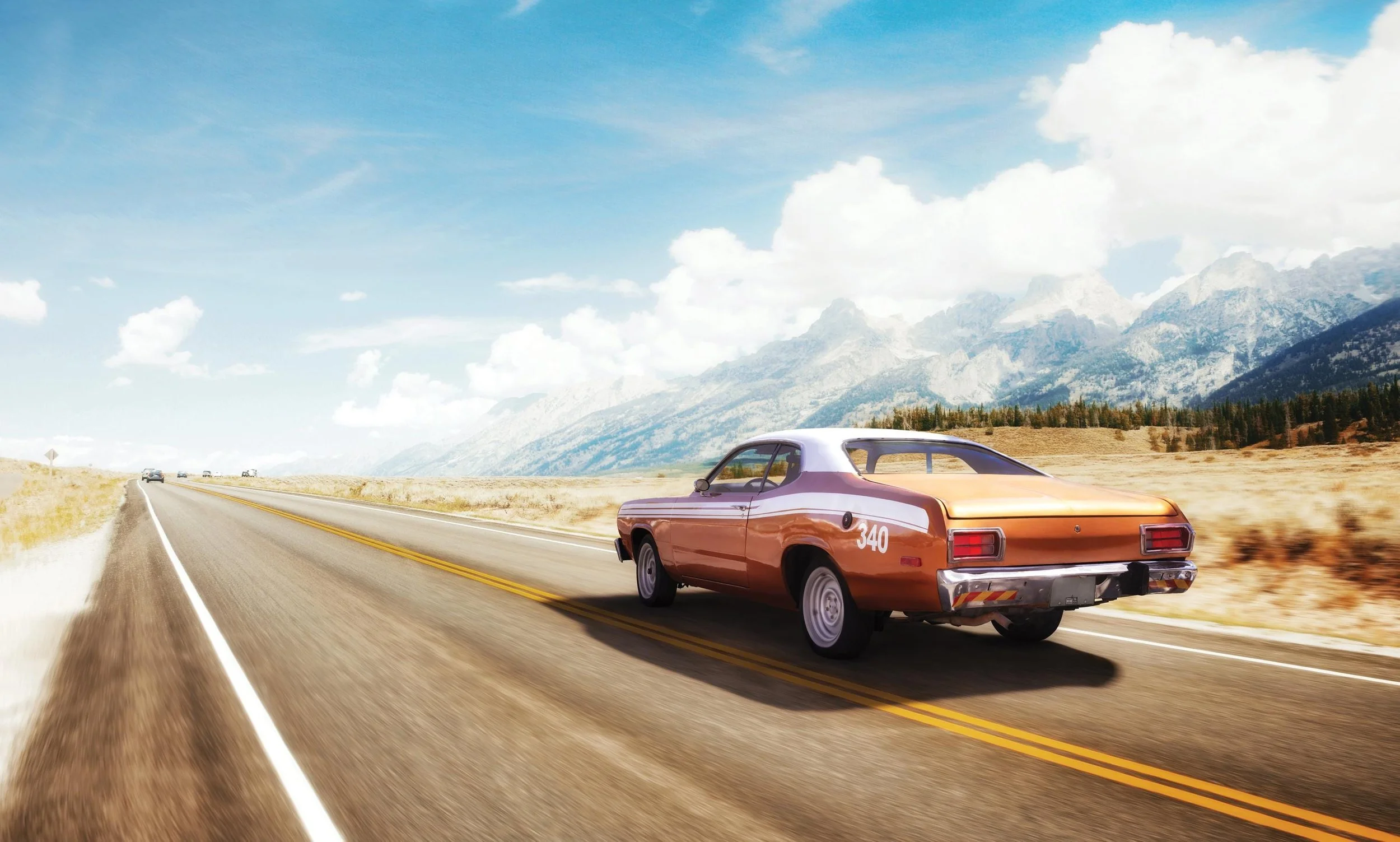 A vintage orange car driving on an open highway through a mountainous landscape under a blue sky with clouds.