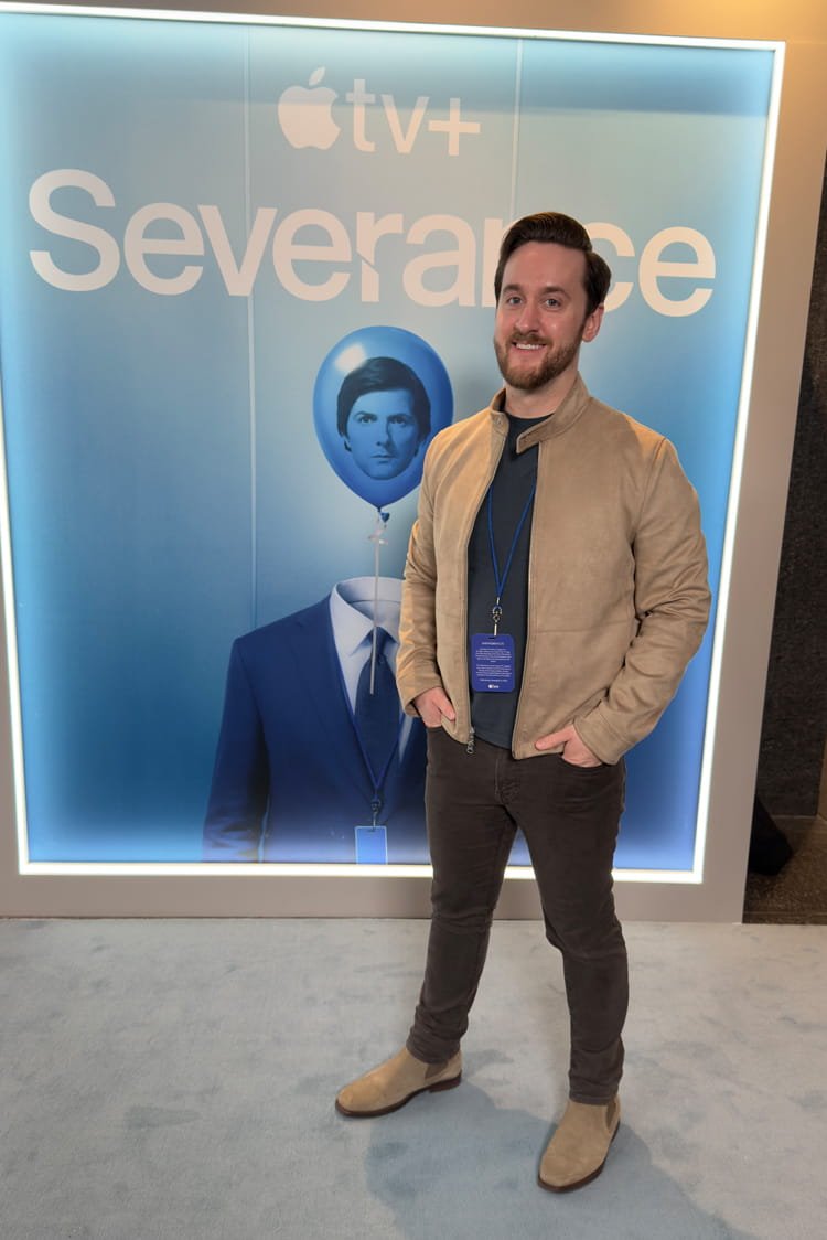 A man standing in front of a large Apple TV+ advertising display, which features the show "Severance" and an illustration of a man with a balloon head with a face.