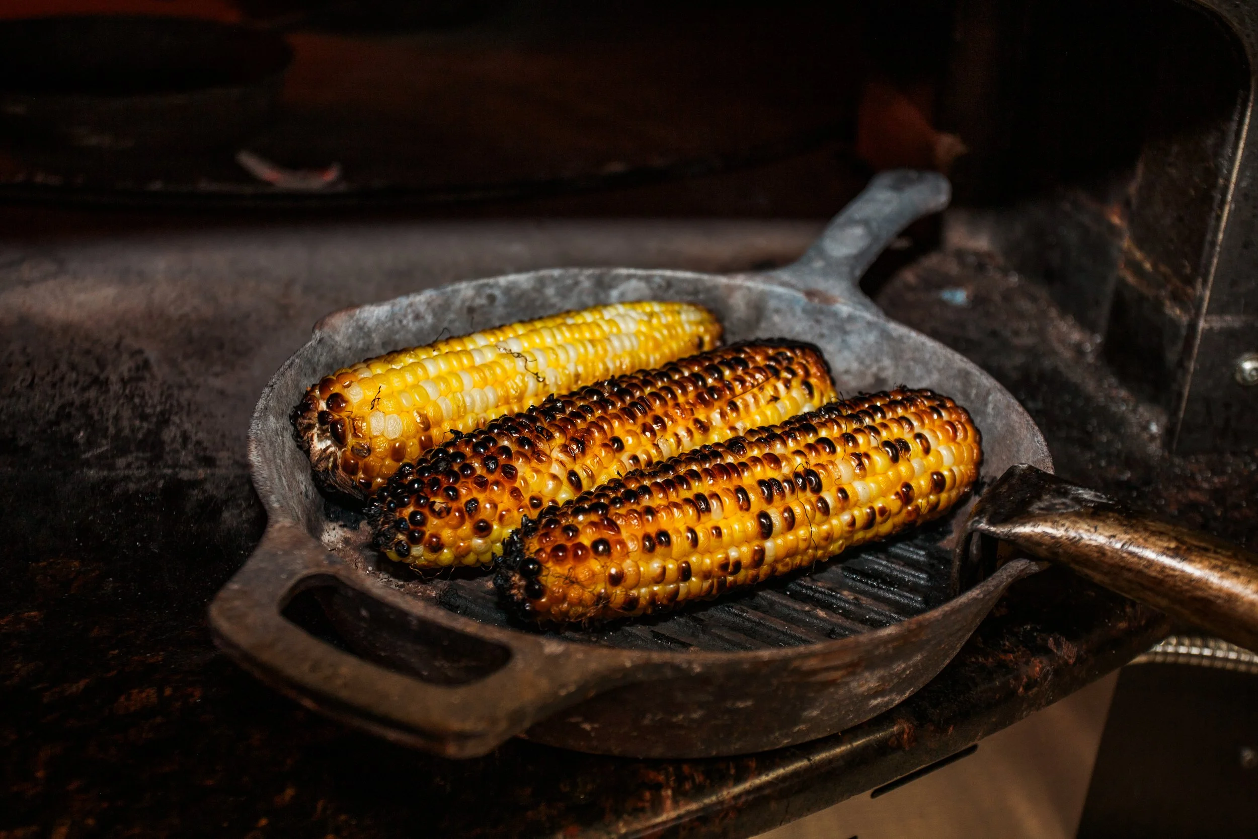 Three ears of corn, some with blackened kernels, roasting on a grill inside an oven.