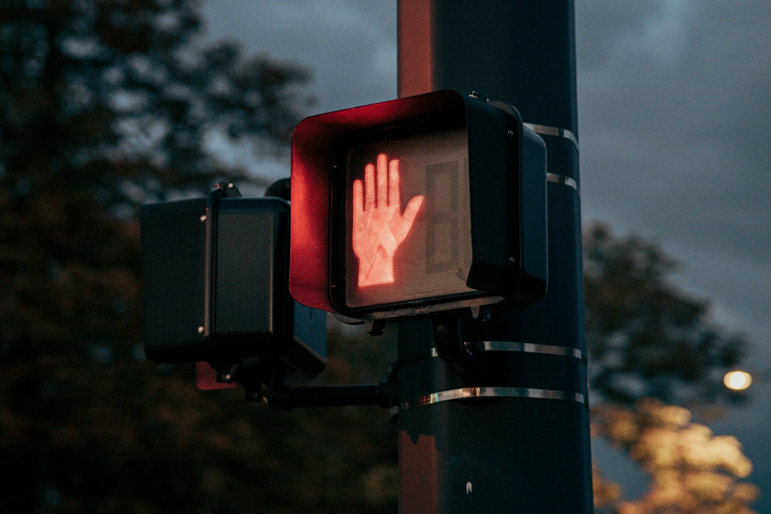 Red pedestrian crossing signal with a raised hand icon, indicating 'stop' or 'do not walk', mounted on a pole at night.