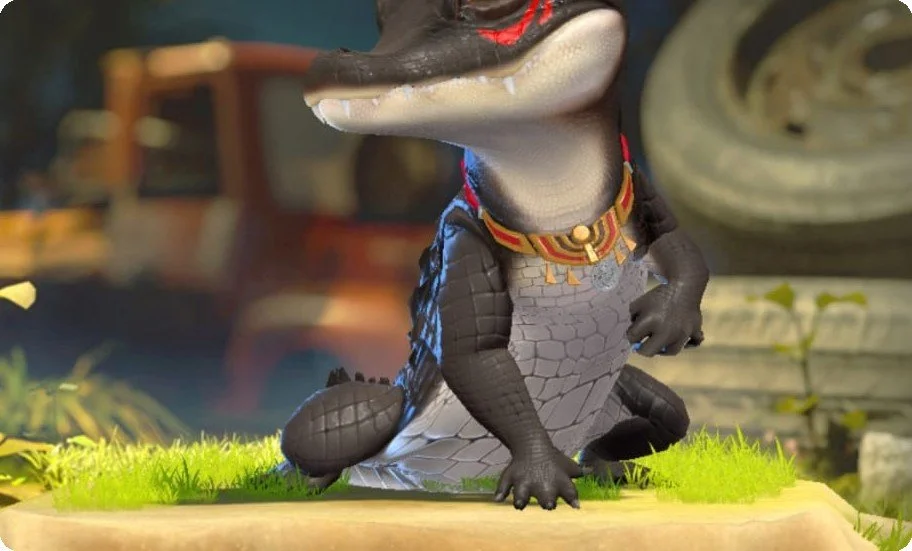 Close-up of a toy creature resembling a crocodile dressed as a superhero, sitting on green grass with a toy vehicle in the background.