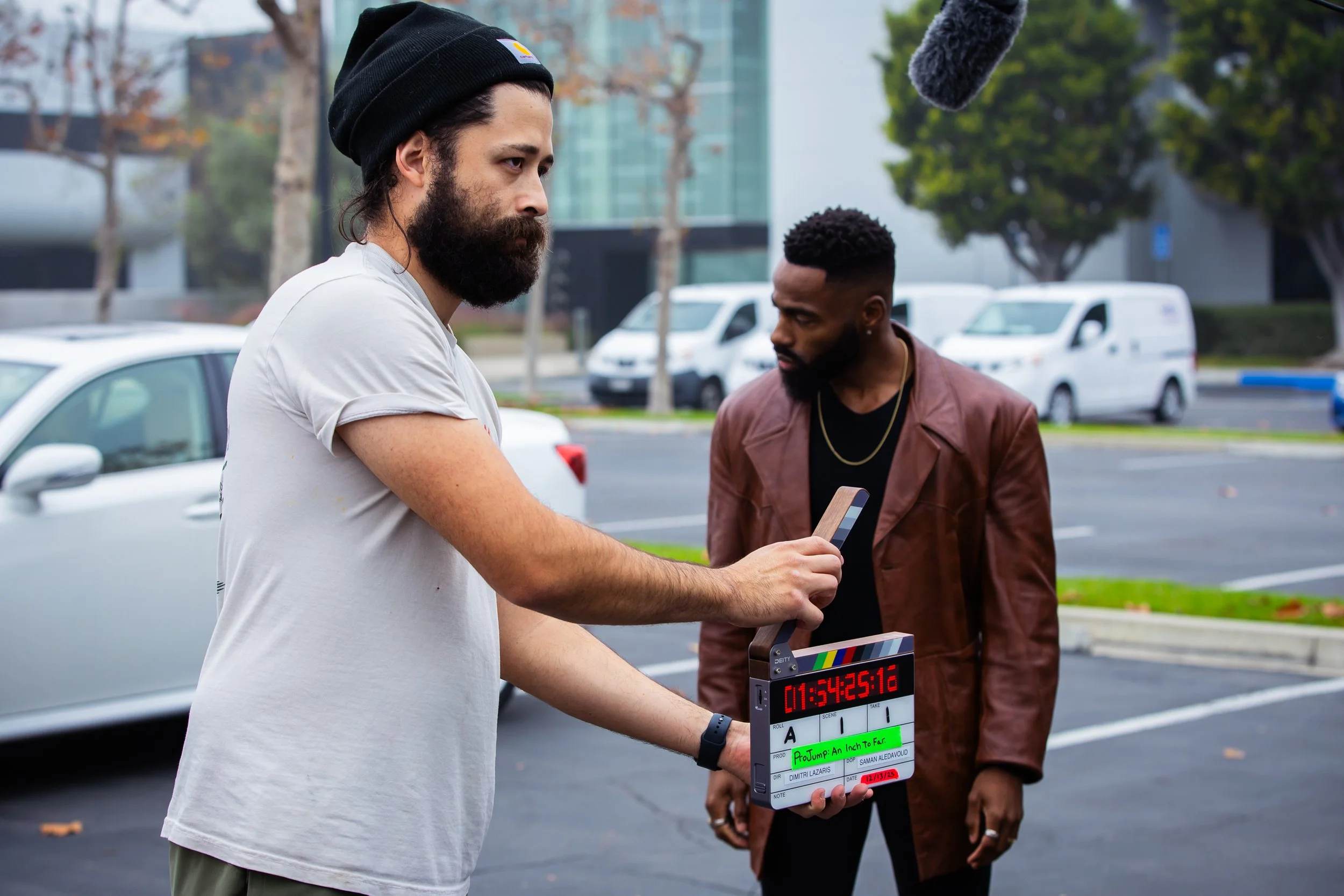 A crew member present a slate to a camera to begin rolling. An actor prepares behind him.