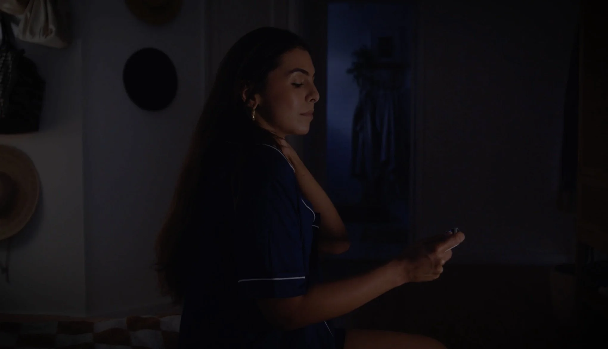 A woman sits on the edge of a bed in the middle of the night looking at a baby monitor.