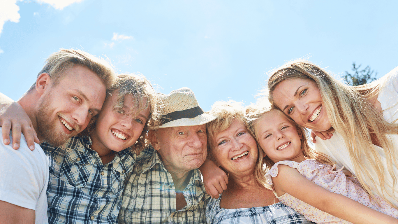 a multigenerational family with grandparents, parents, and two kids taking a selfie in the backyard of their multigenerational house