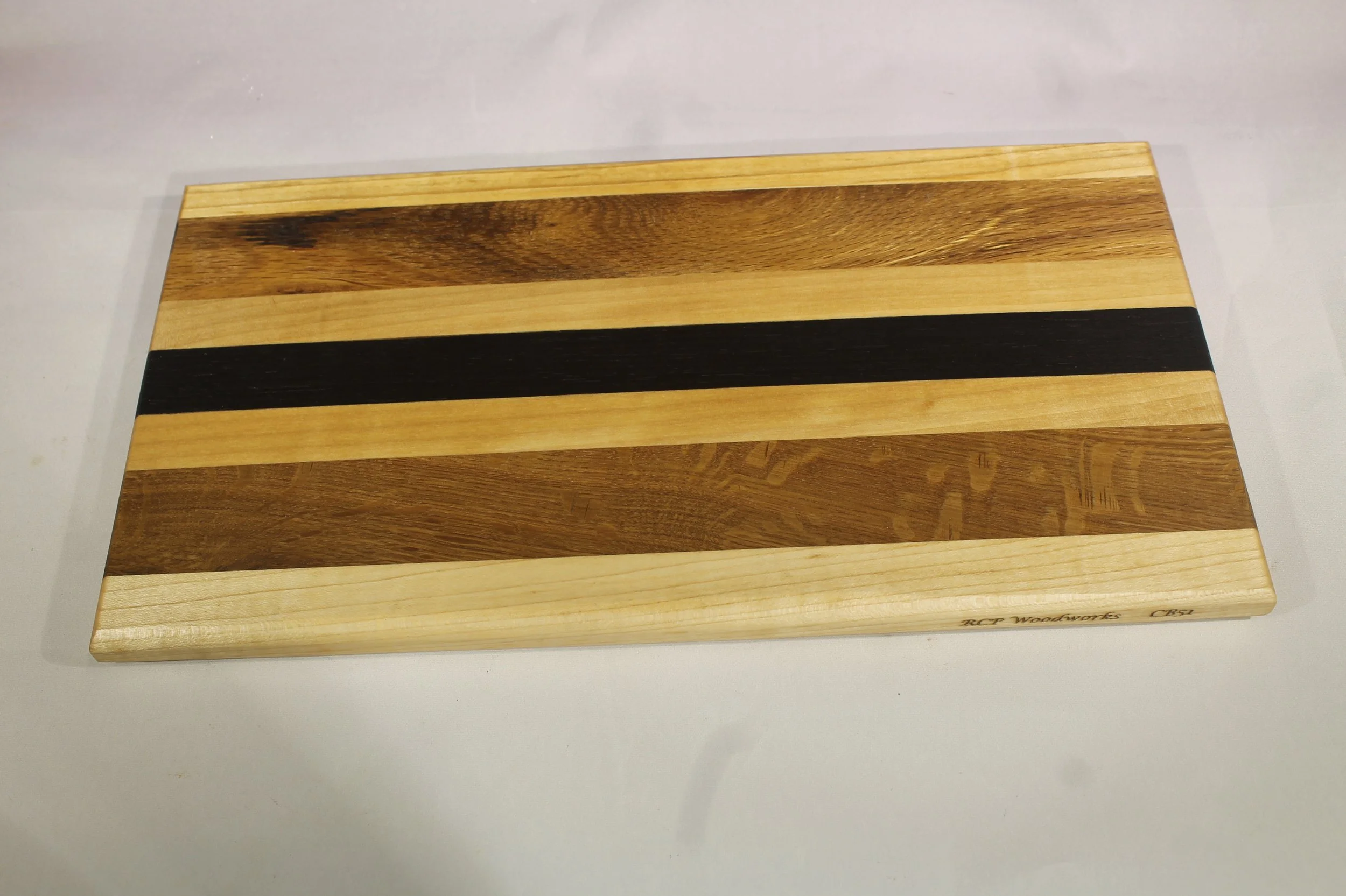 CB51 -  Charcuterie board.

6 ¾” wide by 12 5/8” long by 11/16” thick.
Seven segments of wood – Maple, Oak, Maple, Wenge, Maple, Oak, Maple.

Finished with cutting board oil.       $55

